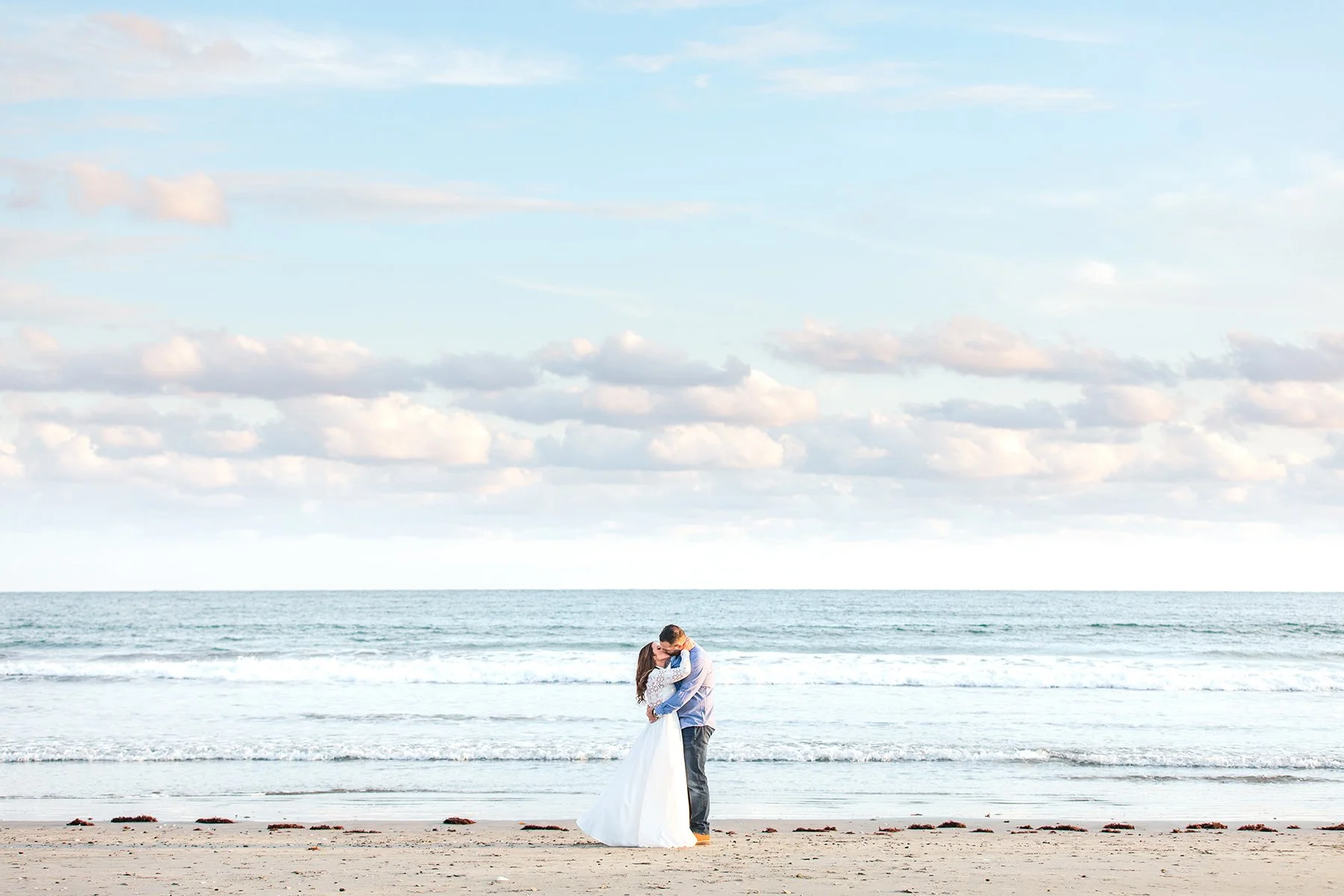 A couple embracing on the beach with the ocean and sky in the background.