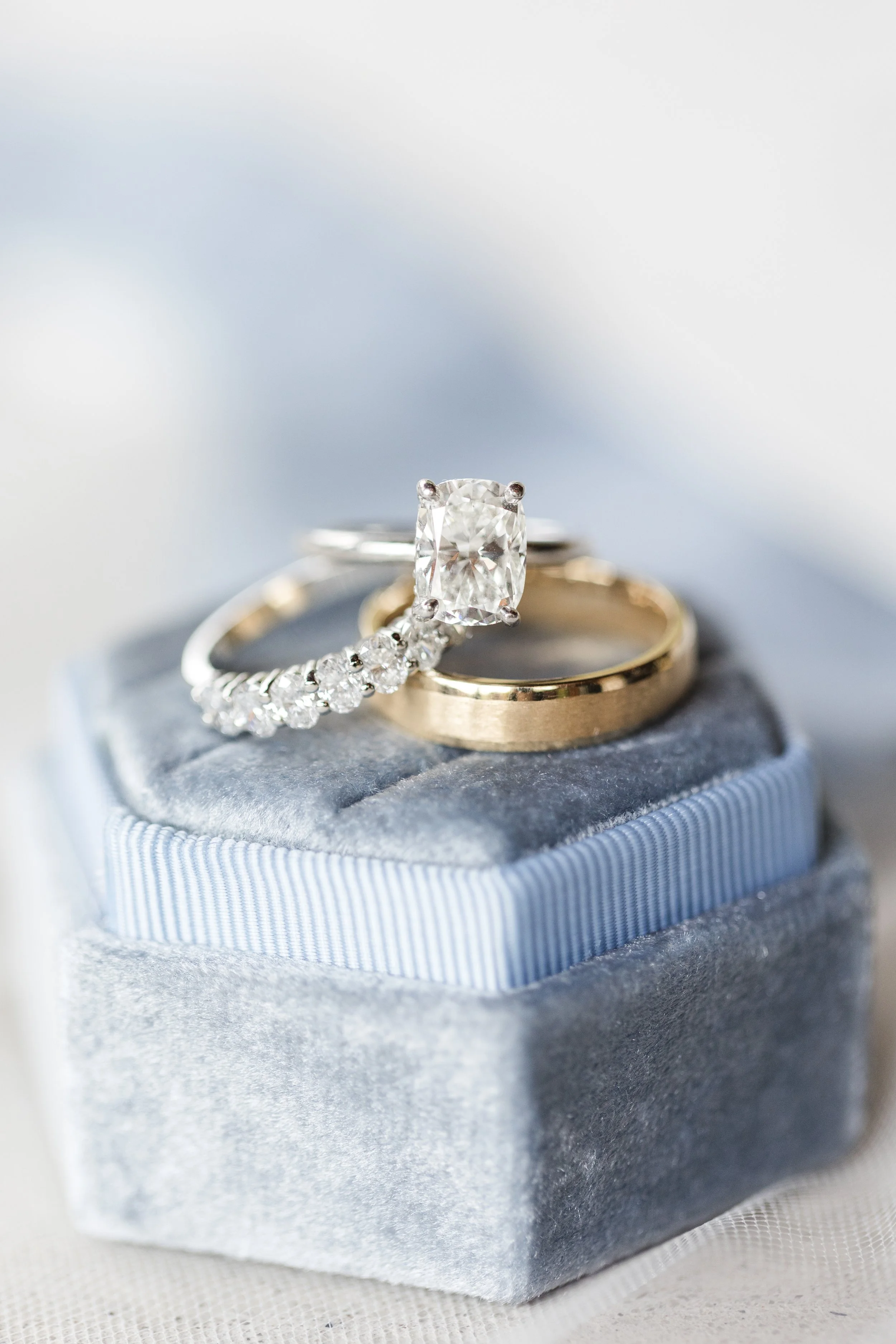 Close-up of three rings resting on a velvet jewelry box. One ring has a large rectangular diamond, another is a gold band, and the third is a diamond-studded engagement ring.
