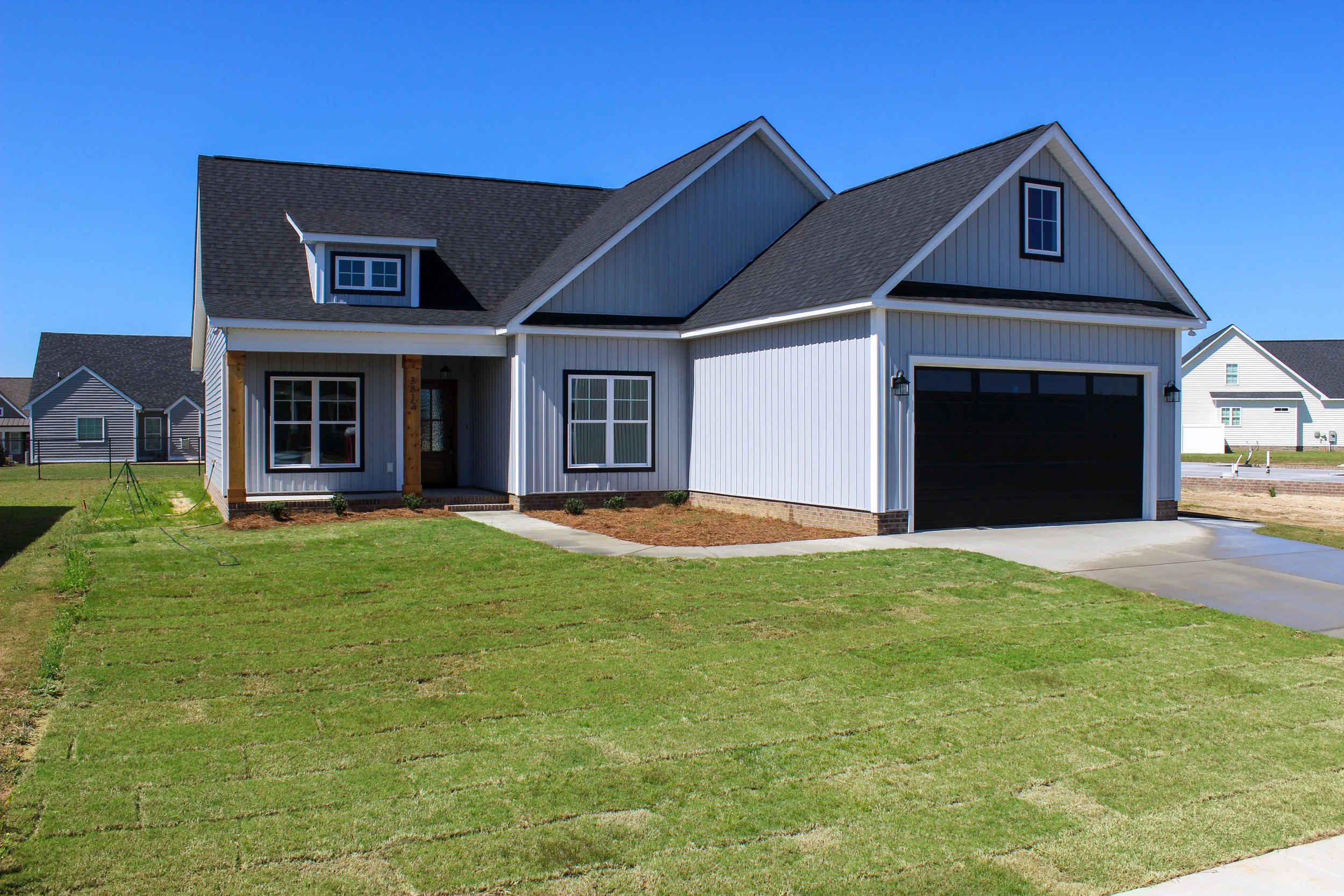 Newly built white house with black garage door, black window frames, and gray gable roof in a suburban neighborhood.