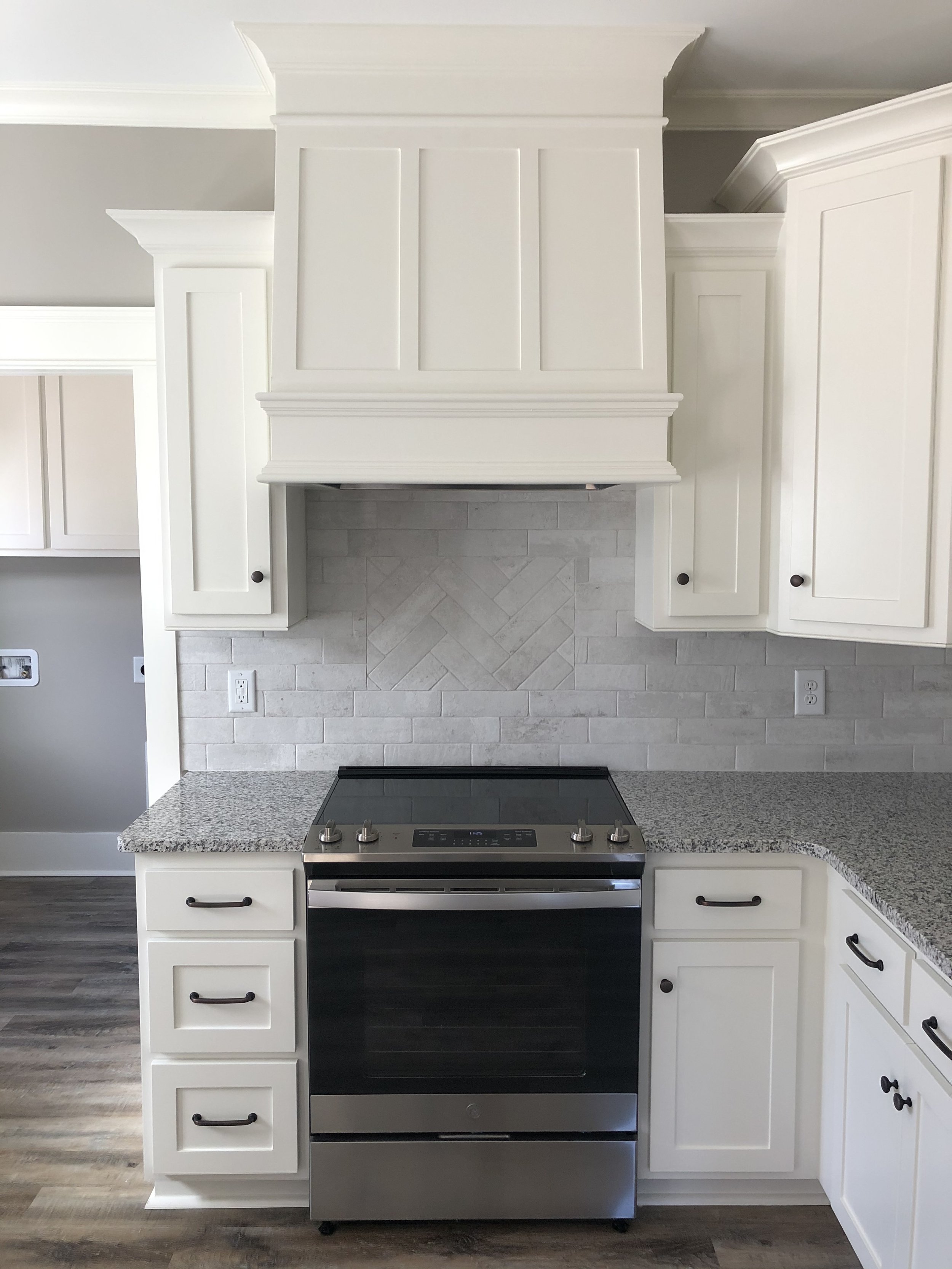 Modern kitchen with granite countertops, white cabinets, stainless steel oven, and gray brick backsplash.