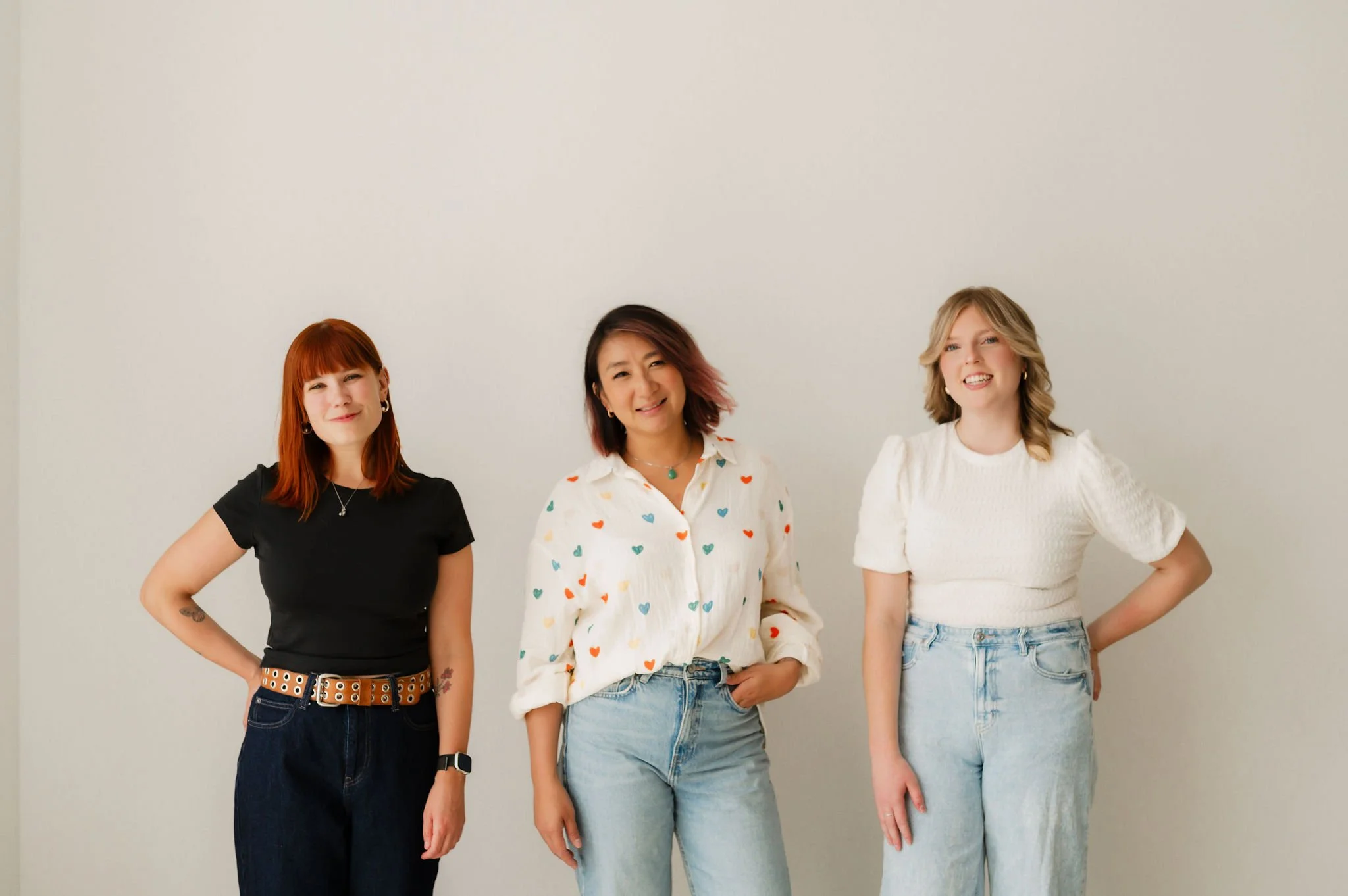 Three women standing in front of a plain white wall, smiling at the camera.