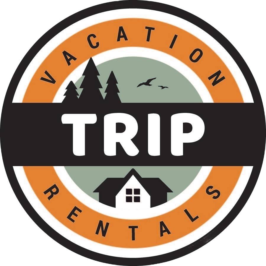 Circular logo with a border. Inside, it says 'Vacation Rentals' at the top and bottom. The center features a silhouette of trees, a house, and flying birds, with a color scheme of green, black, white, and orange.