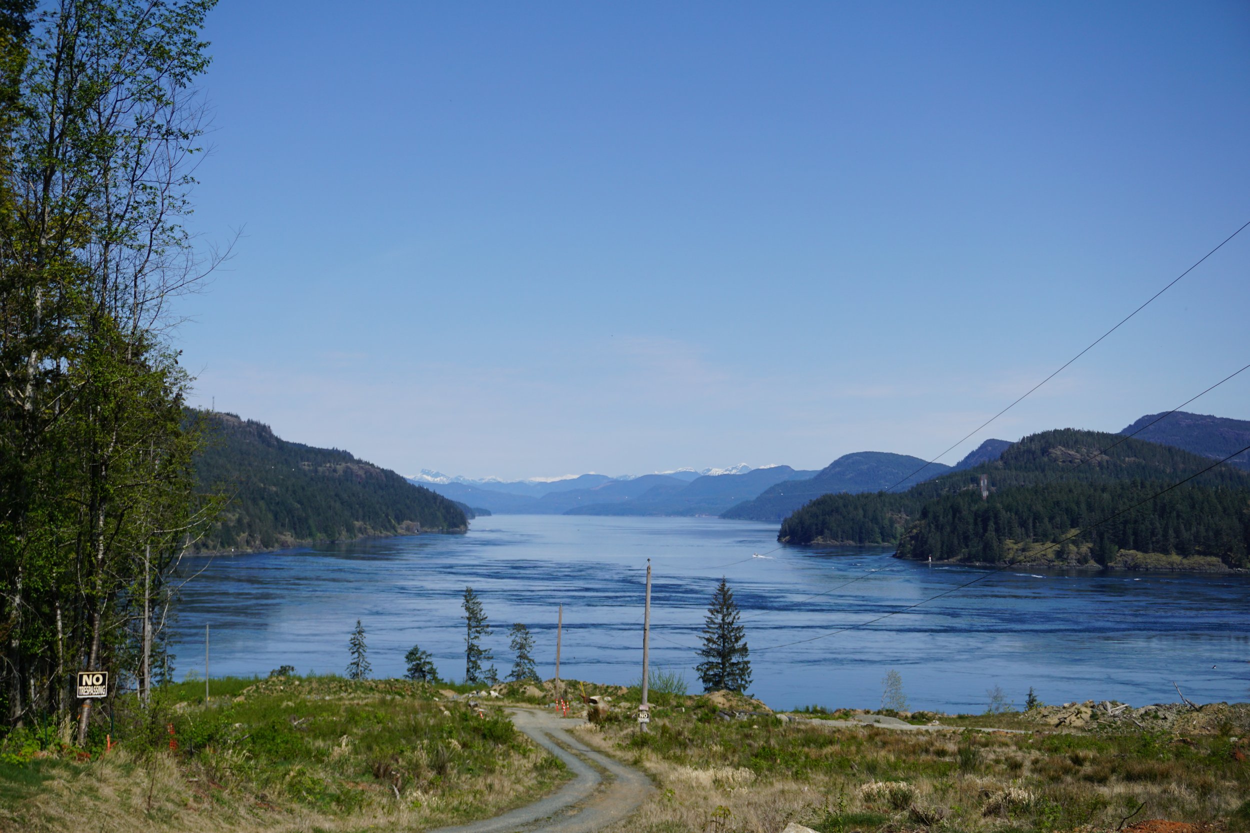 Scenic view of a large river flowing through a lush green valley with mountains in the distance, under a clear blue sky.