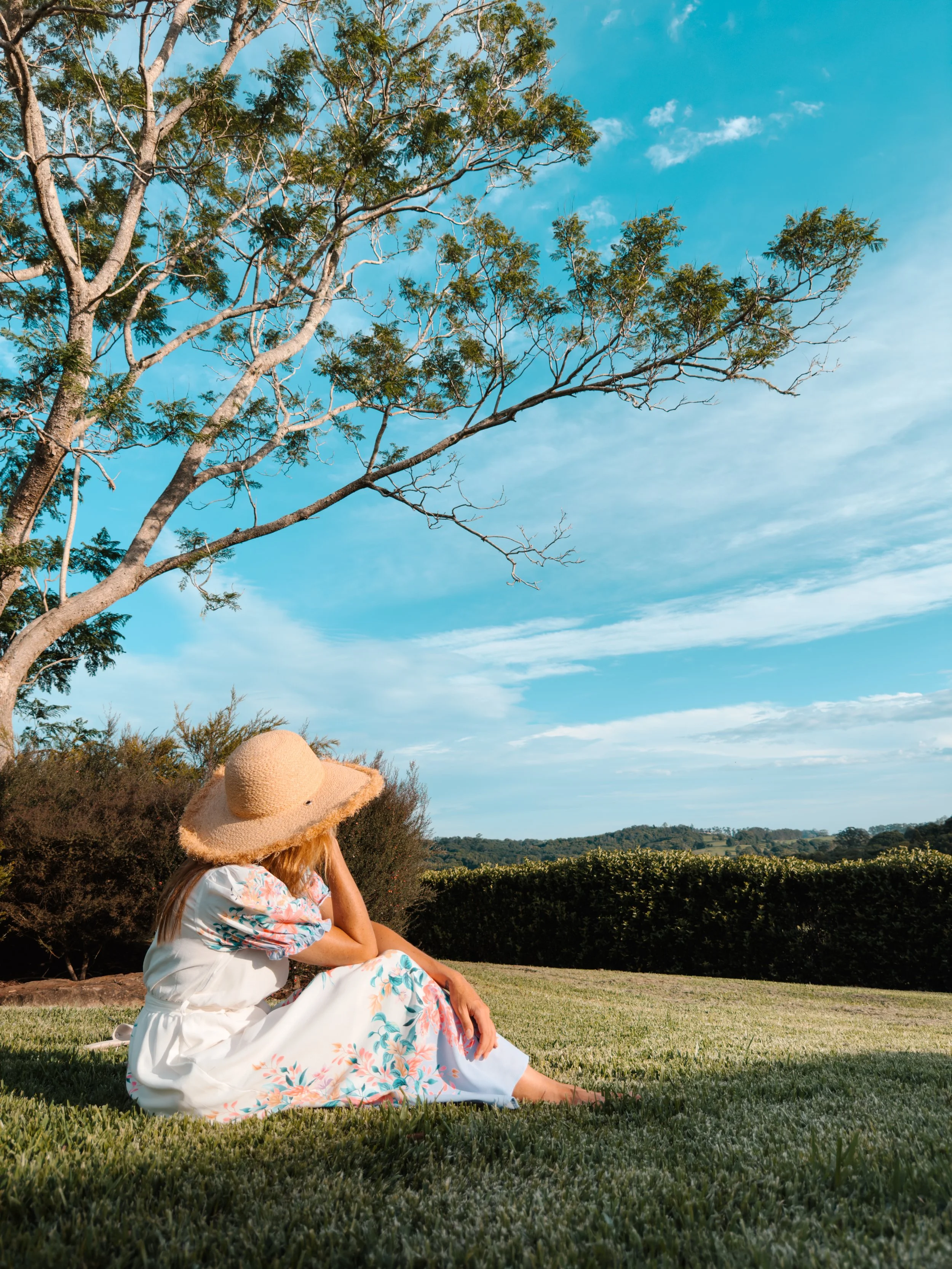 Woman relaxing on open grass overlooking expansive hinterland views at a private retreat in Byron Bay