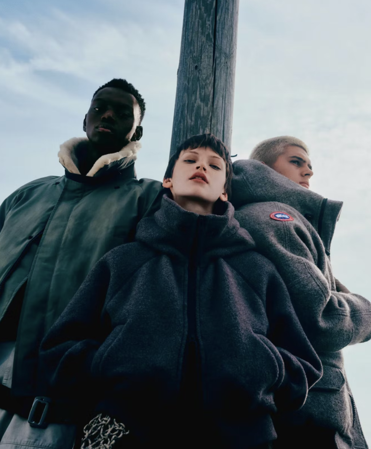 Three young people standing outdoors near a utility pole, looking down at the camera with serious expressions.