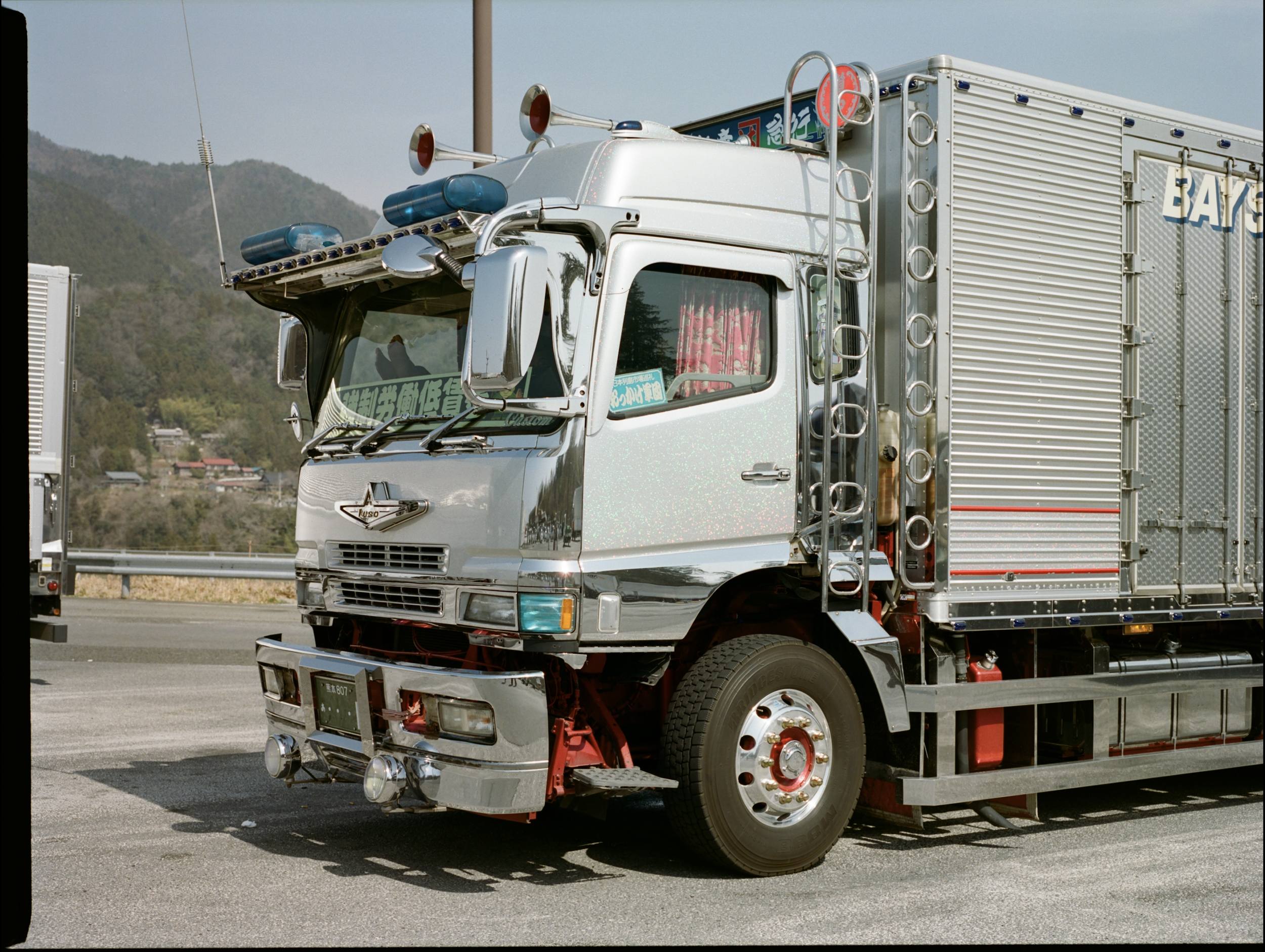 A shiny silver fire truck parked on a highway with a mountainous background.