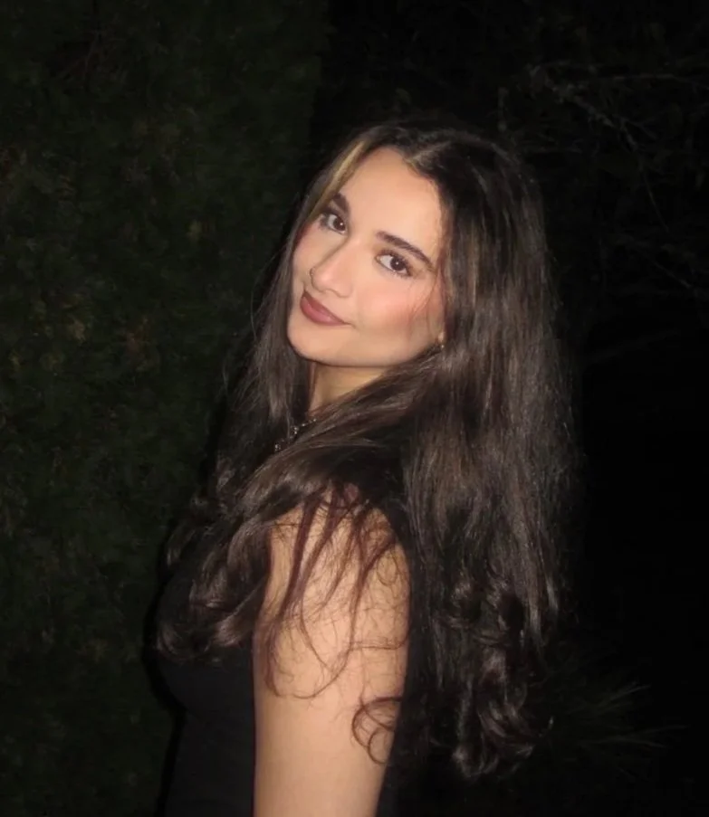 Young woman with long dark hair smiling outdoors at night.