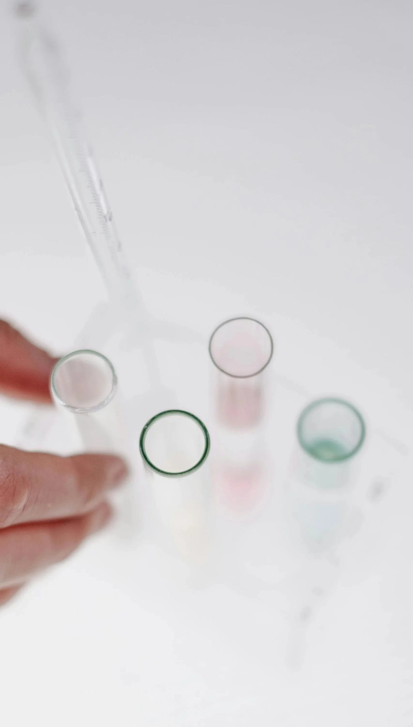 A person's hand holding a glass test tube, with three other test tubes in the background on a white surface.