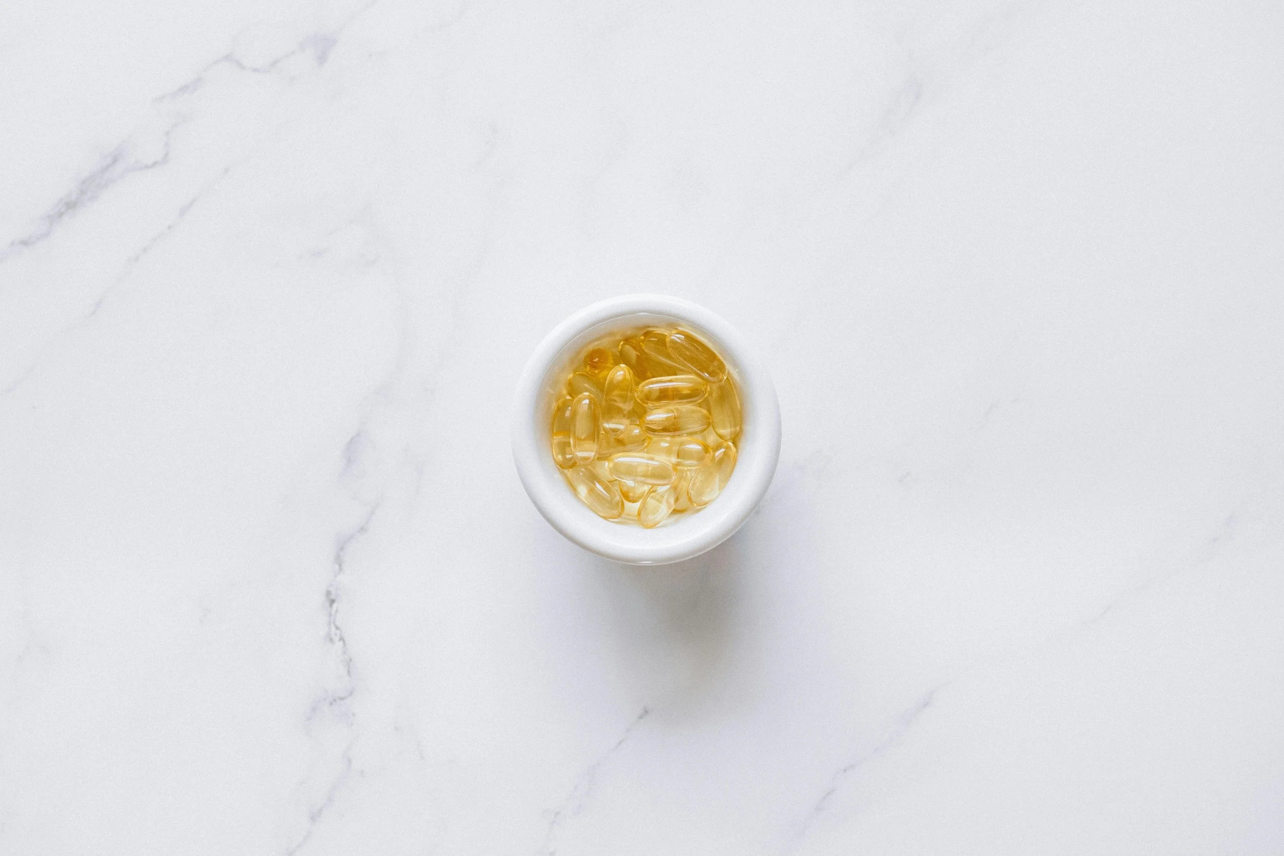 A white cup filled with yellow softgel capsules on a white marble surface.