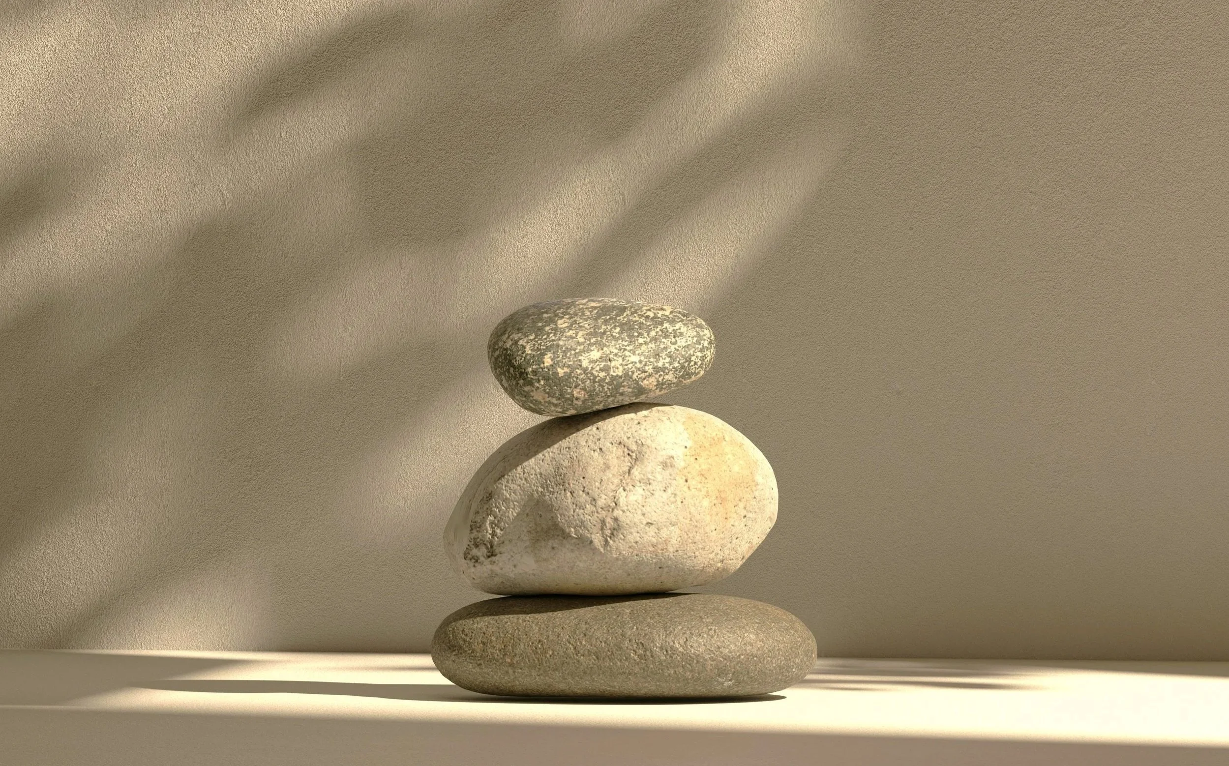 A stack of four smooth stones placed on a flat surface, with shadows cast on a beige wall behind them.