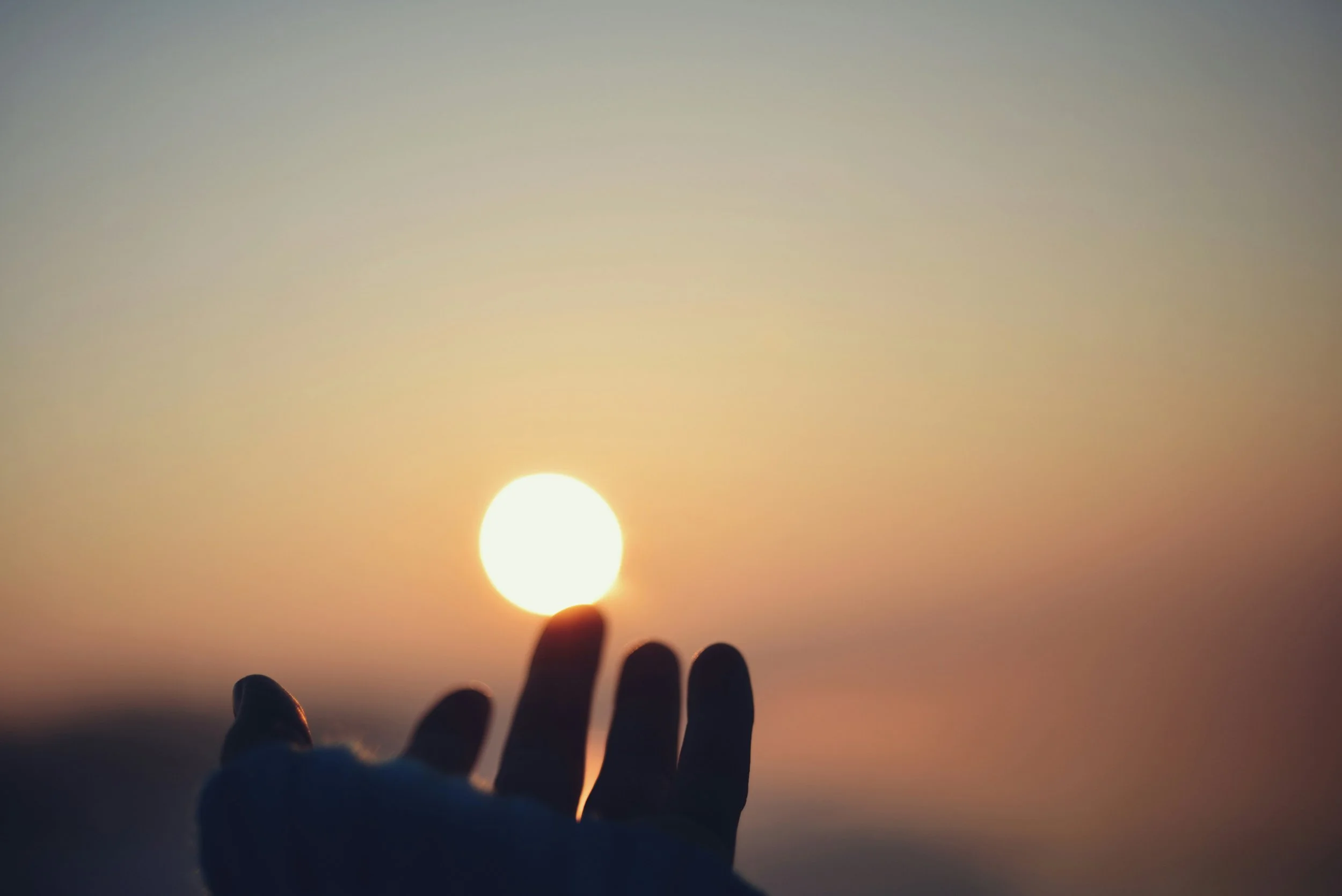 Hand reaching out towards the setting or rising sun, creating a silhouette against the sky.