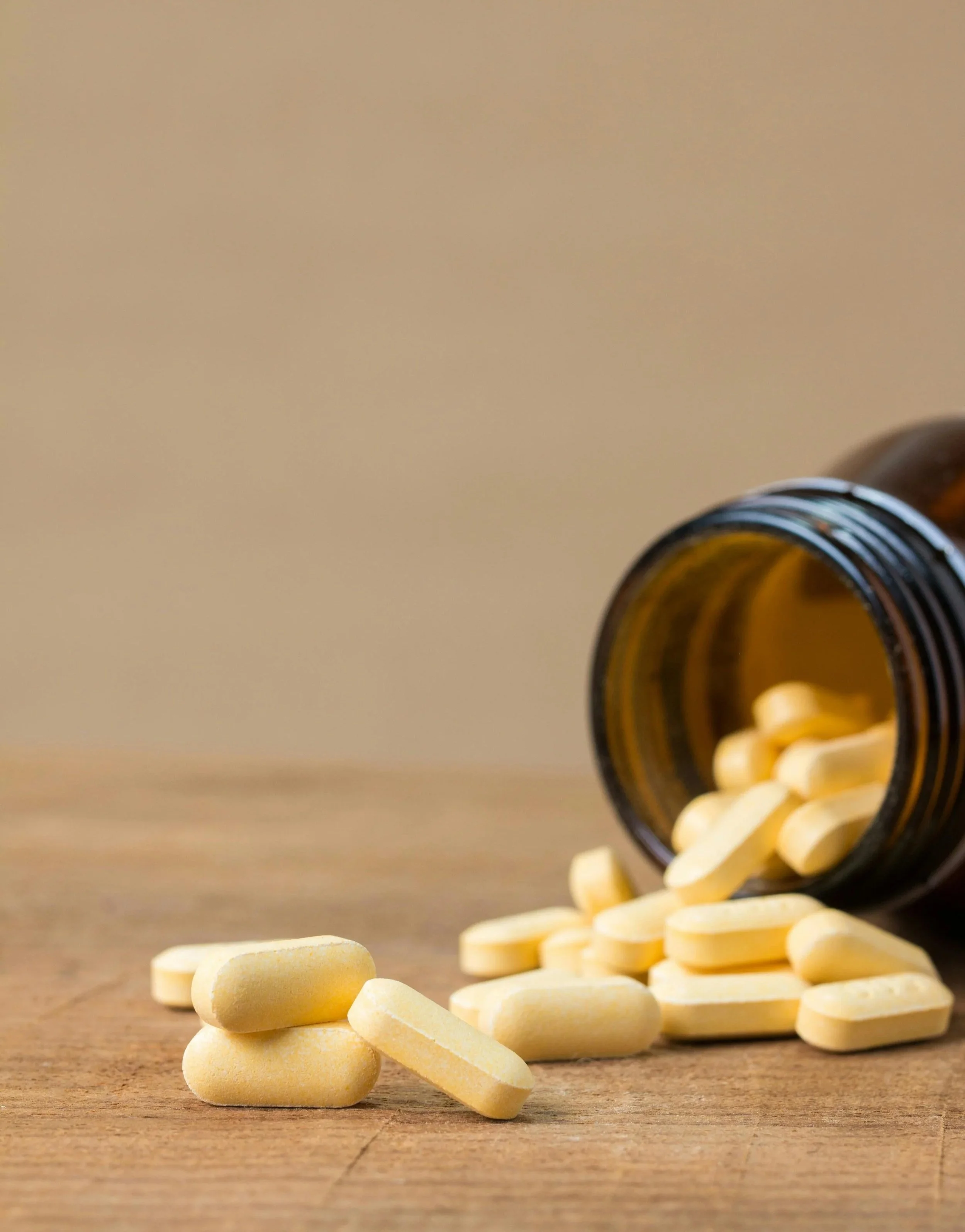 Yellow pills spilling out of an amber medicine bottle onto a wooden surface.