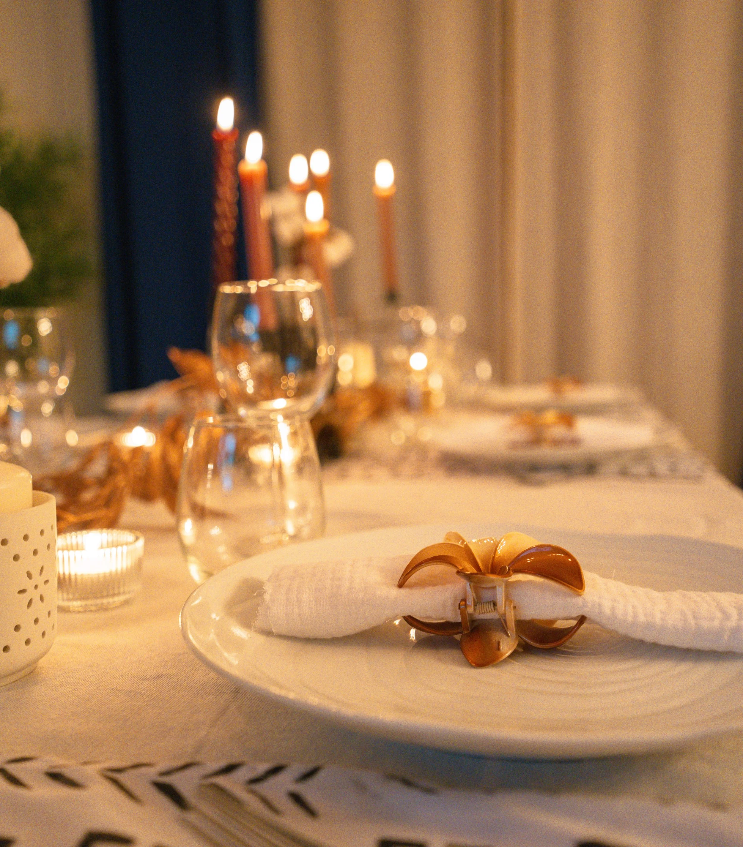 une table de dîner élégante avec une assiette, une serviette, une cuillère en forme de fleur, des verres à vin, des bougies et des chandeliers, ambiance chaleureuse