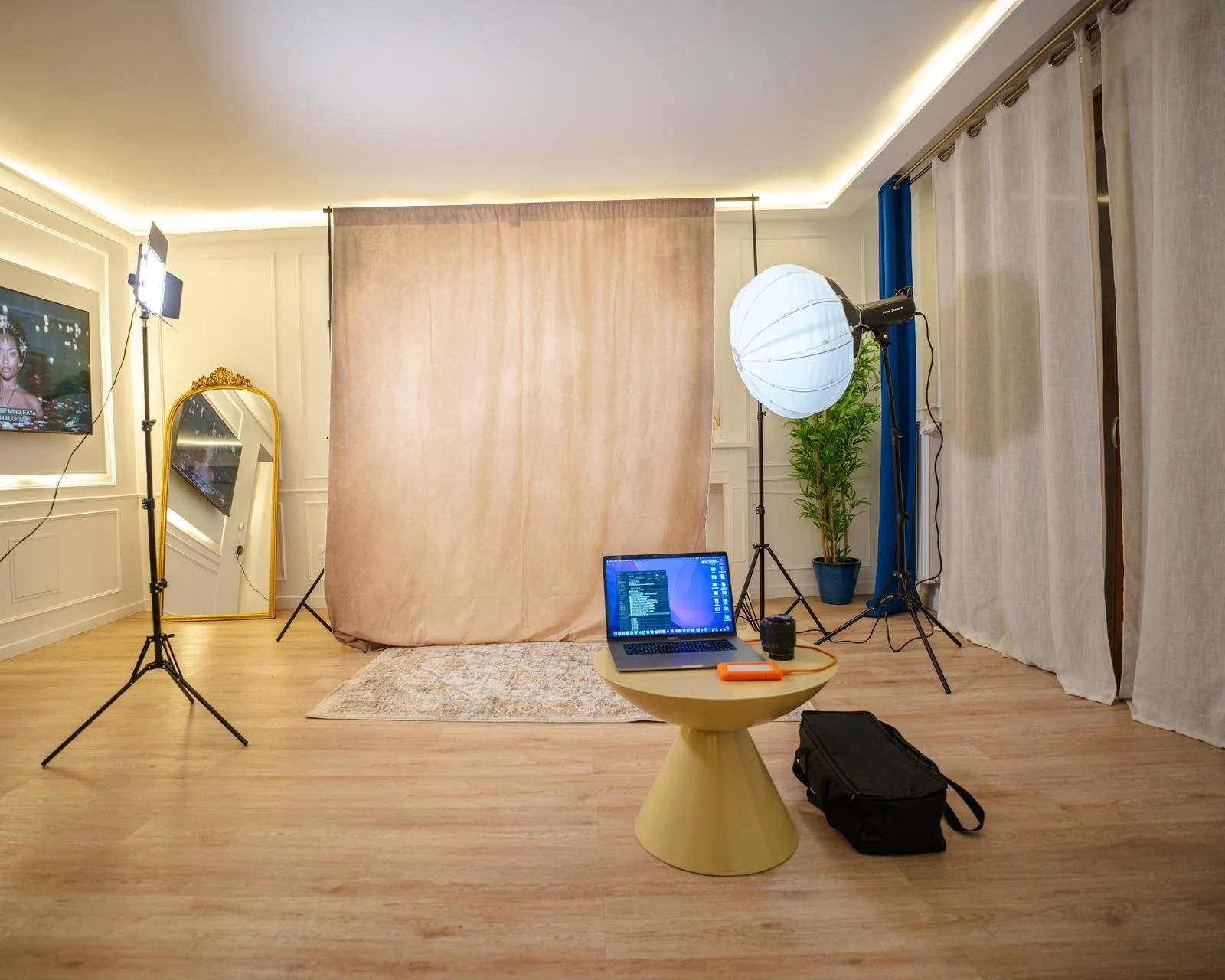 Studio de photographie avec éclairages, fond beige, miroir, ordinateur portable sur une petite table, pellicule, et rideaux blancs.