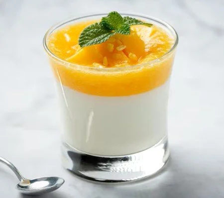 Dessert in a glass with white creamy base, topped with yellow fruit and mint leaves.