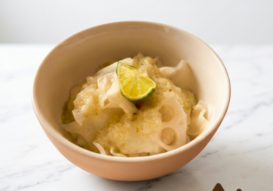 Bowl of soup with lotus root slices, topped with a lime wedge, on a white marble surface.