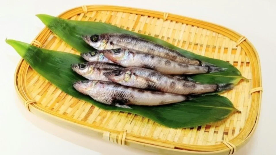 Four small fish laid on green leaves in a bamboo tray.