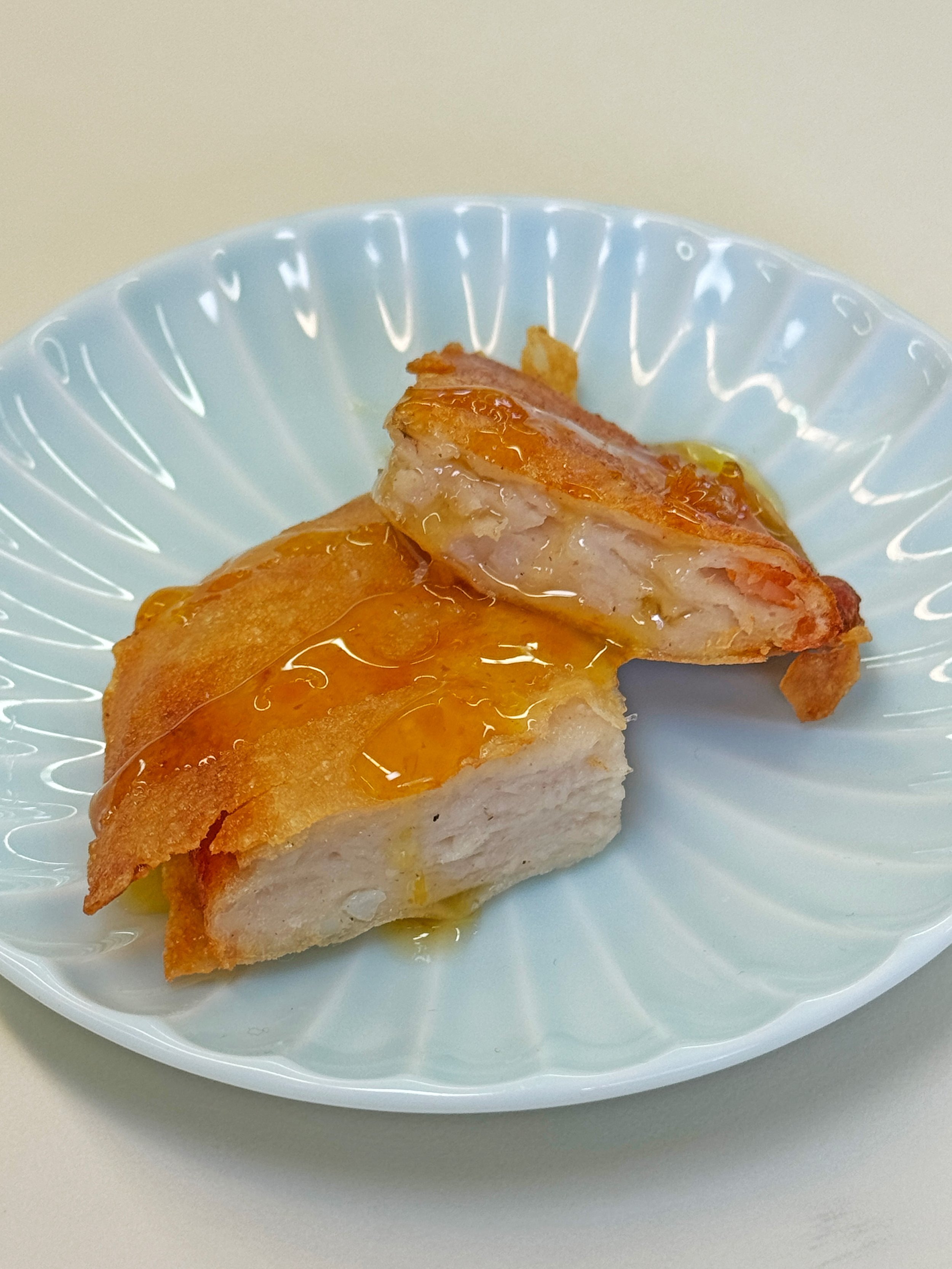 A piece of cooked chicken breast with crispy skin topped with a sauce, placed on a decorative light blue plate.
