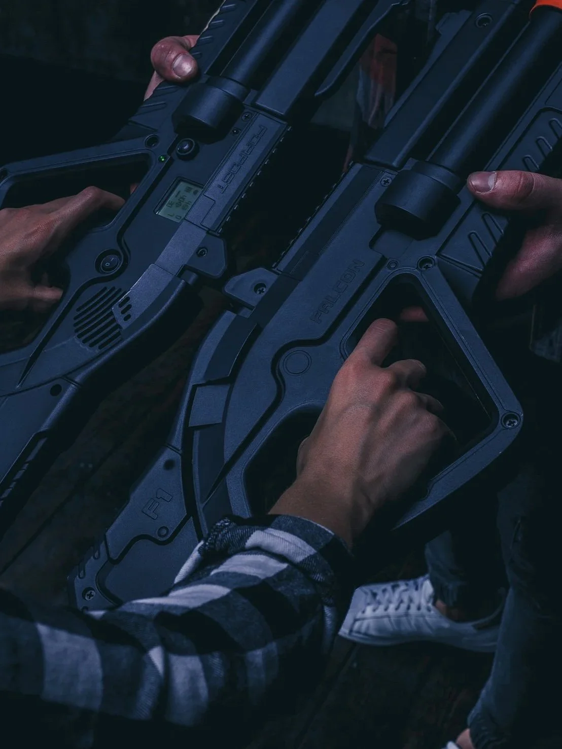 Two people holding futuristic laser guns or weaponry, possibly for a video game or cinematic scene, with one person wearing a plaid shirt and the other person's outfit not fully visible.