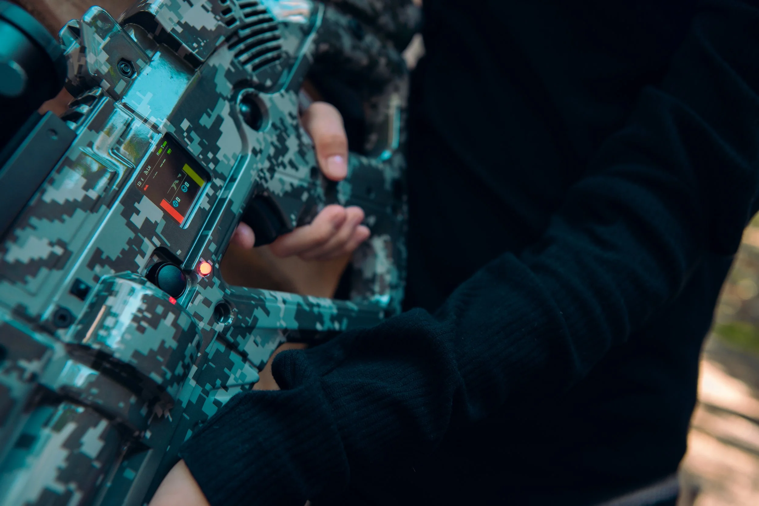 Person holding a remote control device with a digital camouflage pattern, possibly for a drone or remote-controlled vehicle.