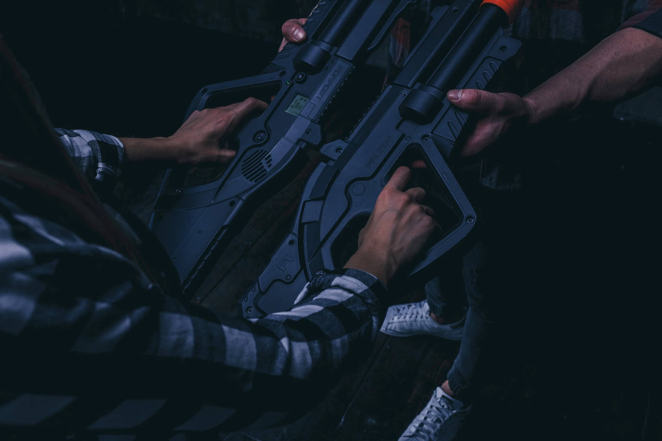 Two people holding futuristic laser guns, one standing and one sitting, in a dark setting.