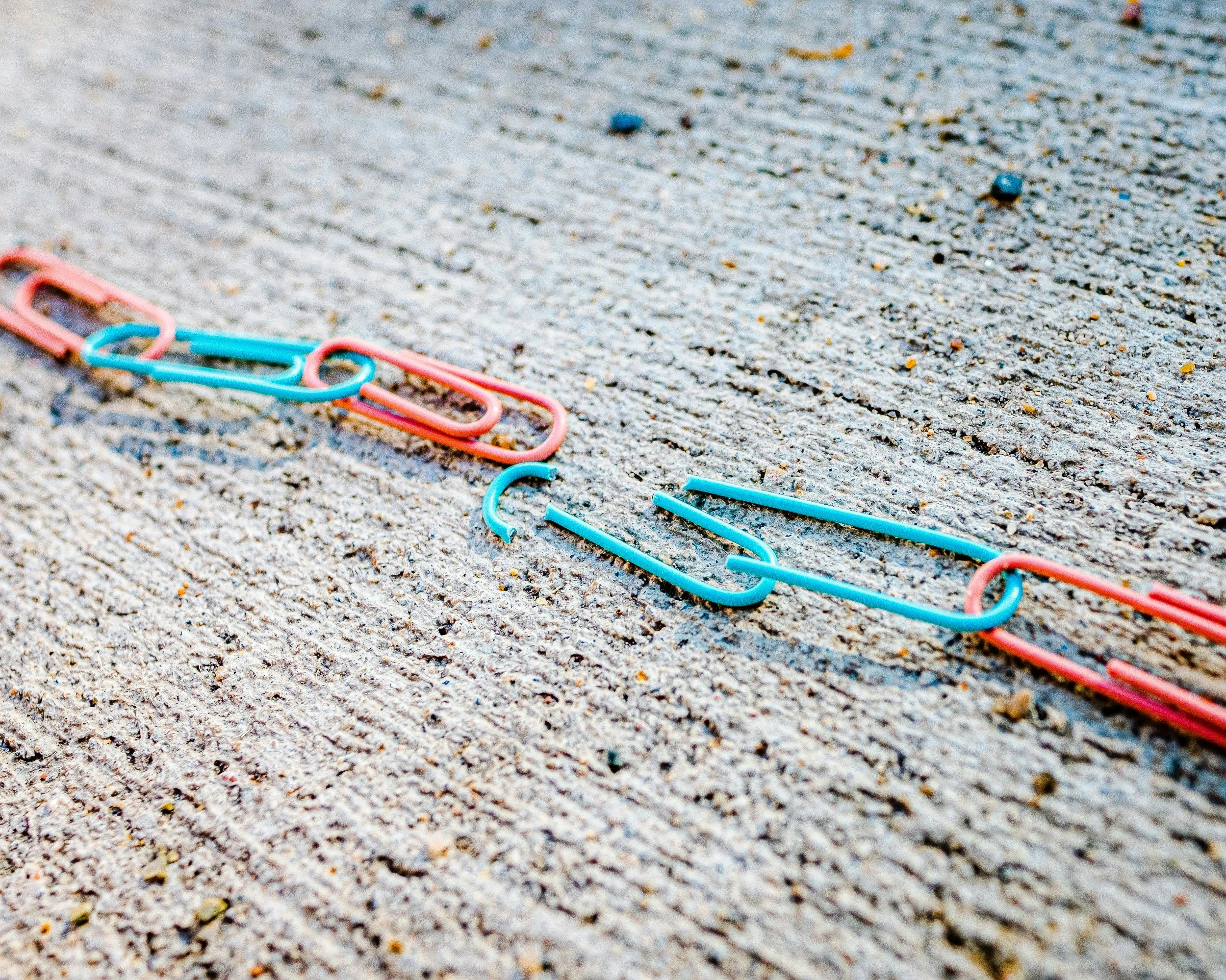 A chain of colorful paperclips with one link broken, symbolizing the disruption of trauma and the process of healing and rebuilding connection in therapy.