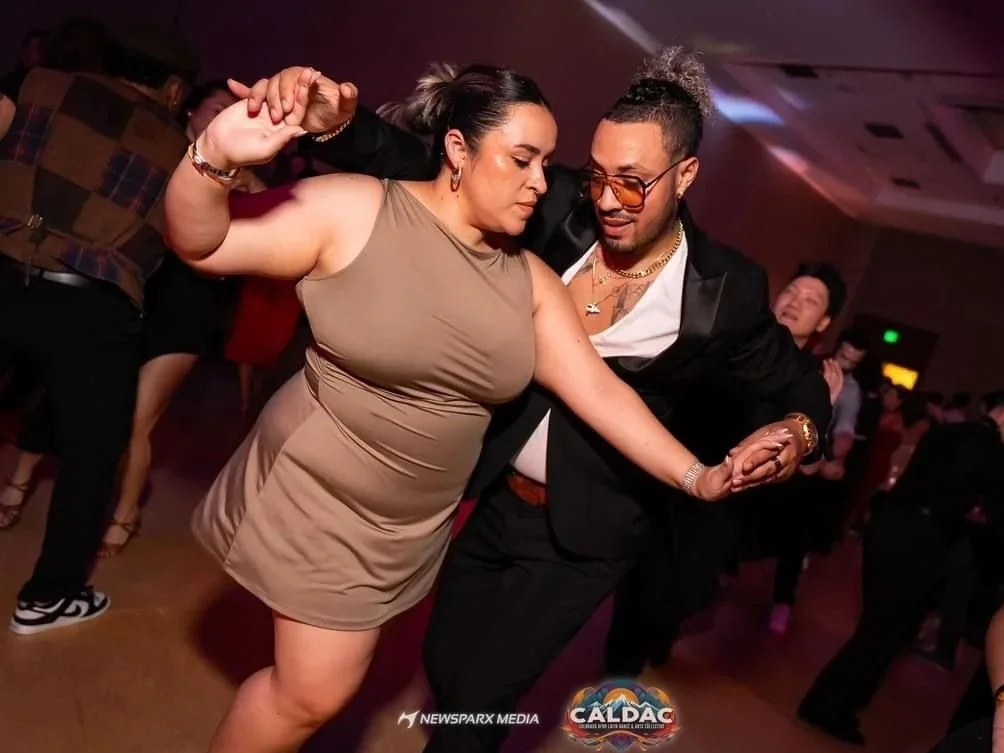 A woman and a man dancing closely at a party or nightclub, with other people dancing in the background.