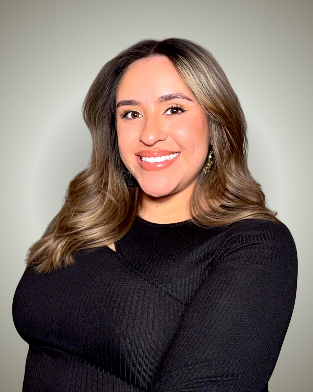 Girl with brown and blonde hair wearing a black long sleeve shirt in front of a white and grey background.
