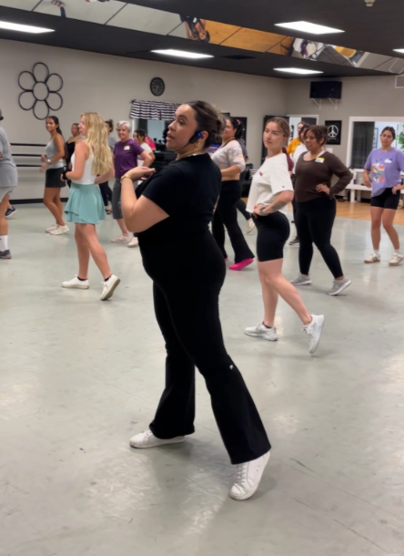 Group of women participating in a dance class in a studio with mirrors and a clock on the wall.