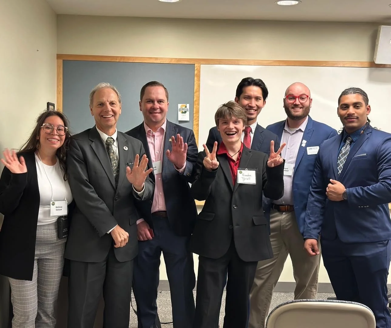 Group of seven diverse professionals at a conference, smiling and posing for a photo in a meeting room.