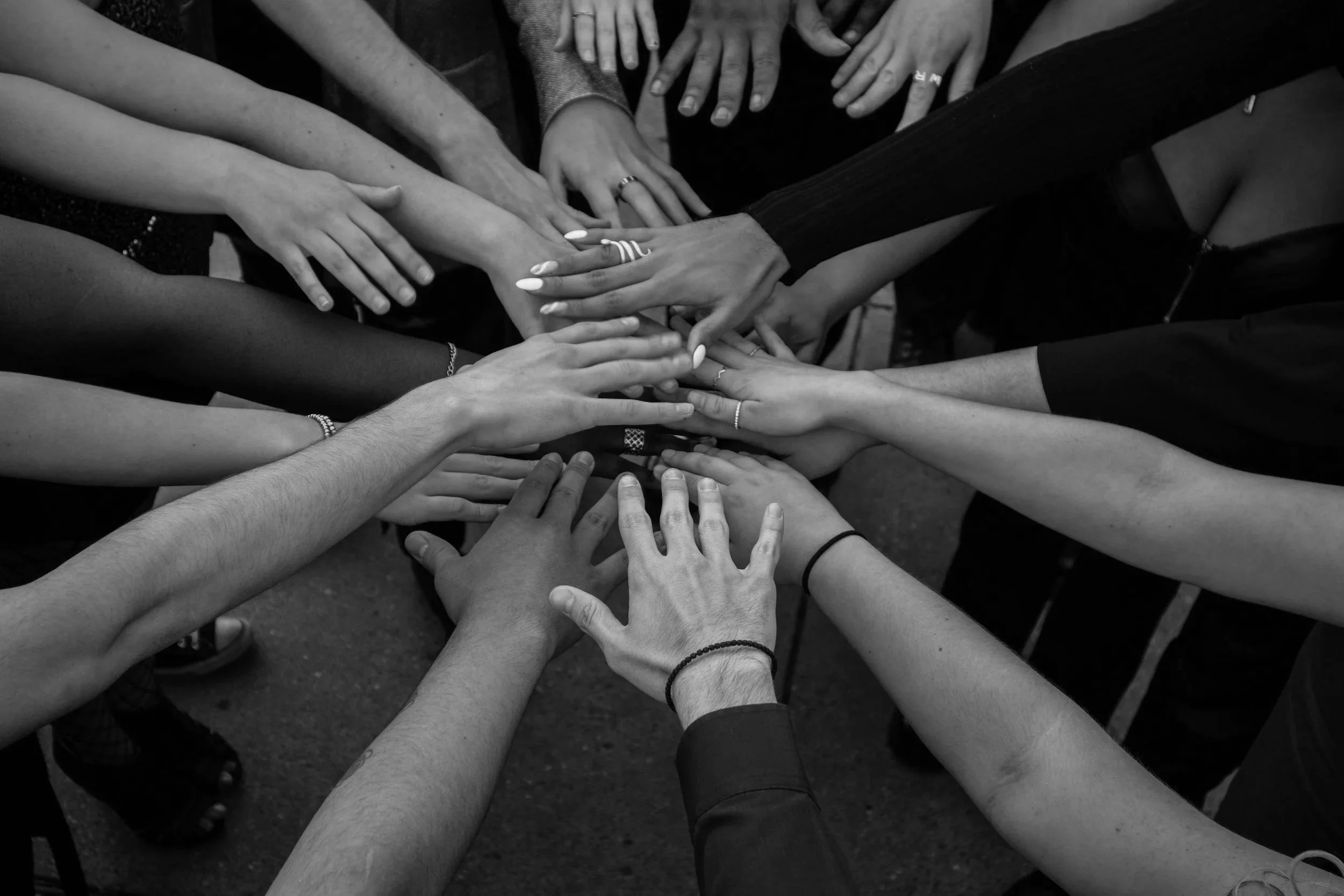 Multiple hands of diverse individuals stacked together in a show of unity or teamwork, black and white photo.