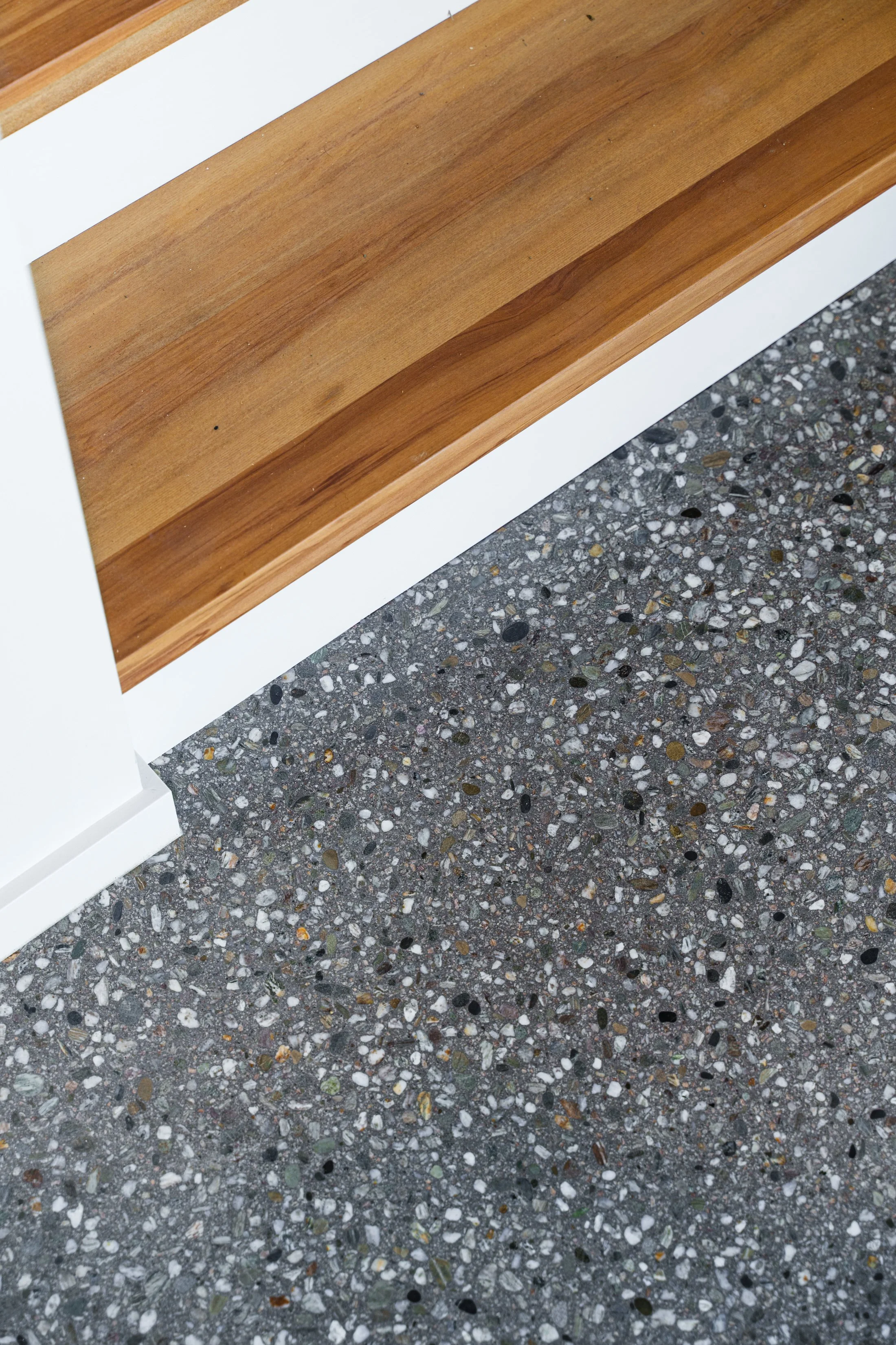 Close-up photo of a wooden shelf resting on a white structure above a speckled concrete floor.