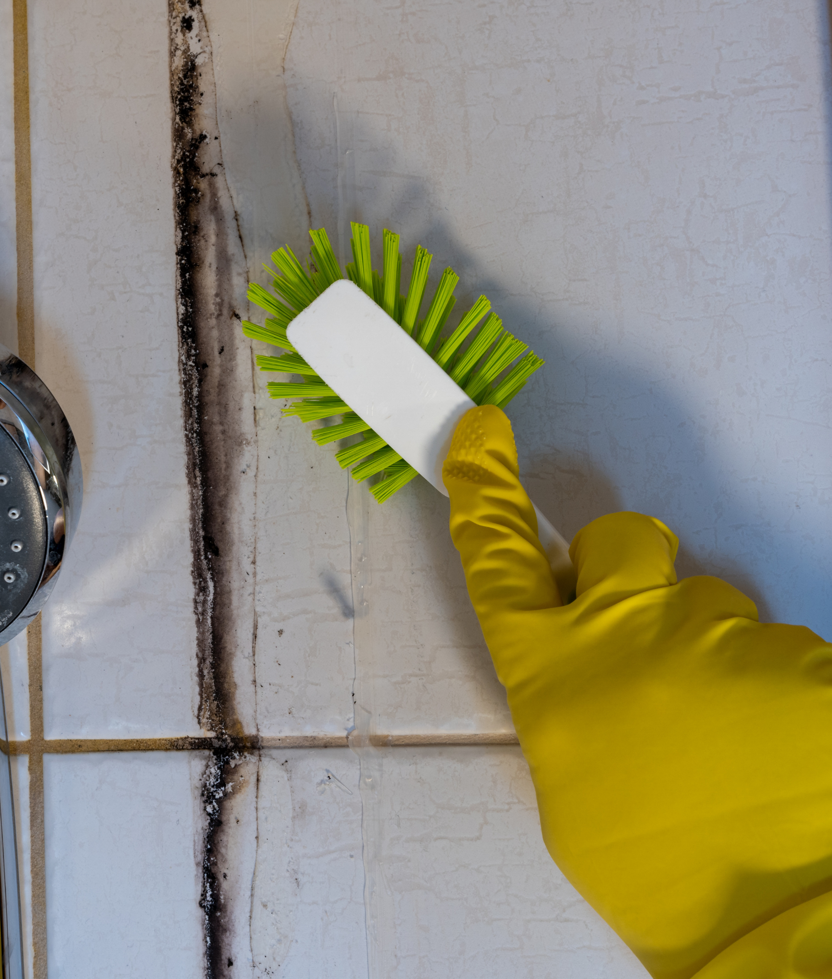 Person wearing yellow rubber gloves cleaning a tiled kitchen surface with a green scrub brush and white sponge.