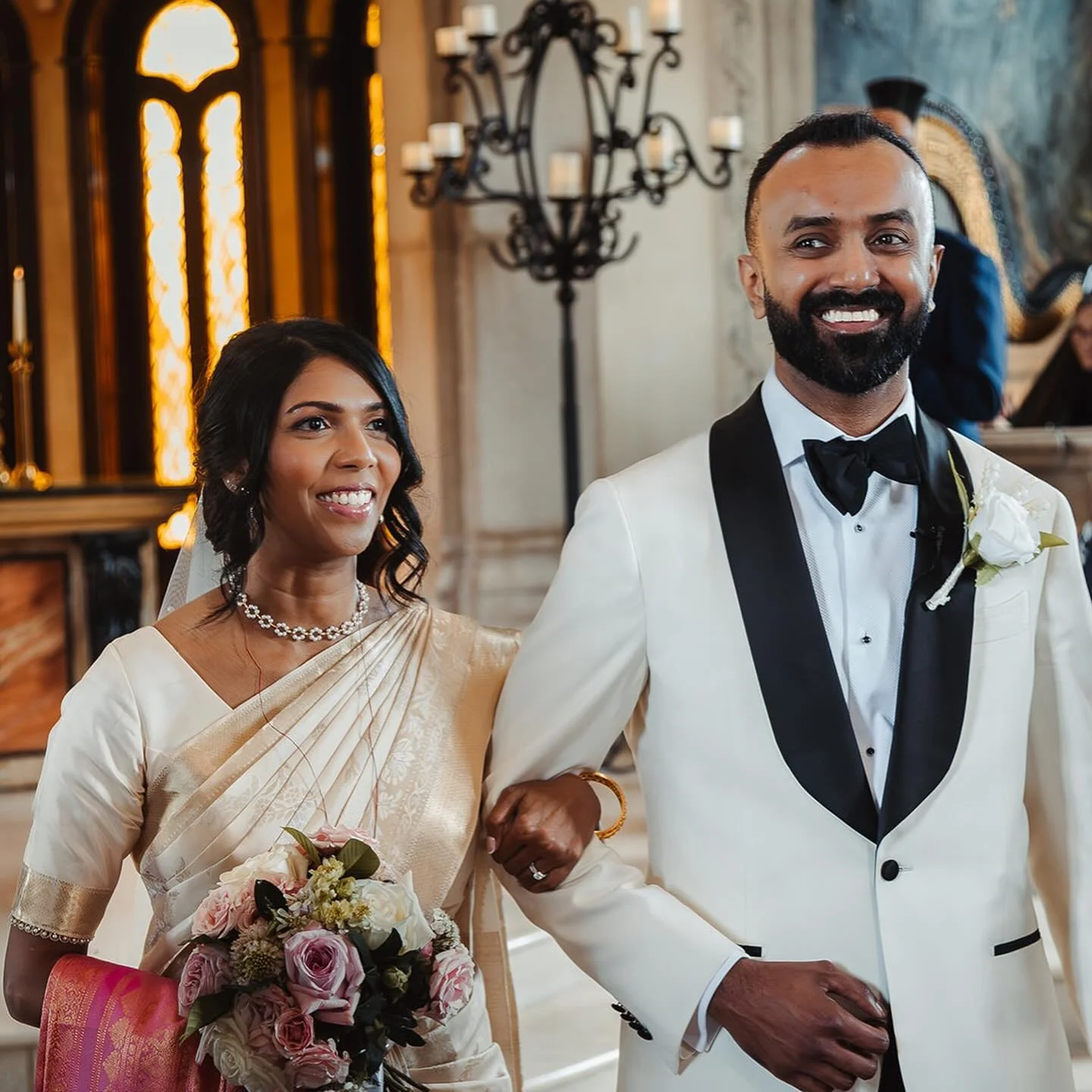 A vision of elegance and joy! We are completely swept away by this beautiful couple. The bride&rsquo;s radiant makeup and sophisticated low updo perfectly complemented her stunning saree and traditional jewelry. The groom&rsquo;s classic white tuxedo