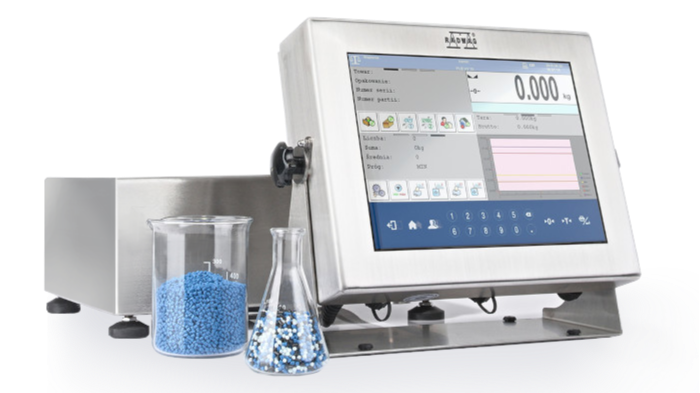 A digital weighing scale with a large touchscreen display next to a beaker and a glass container filled with blue beads.