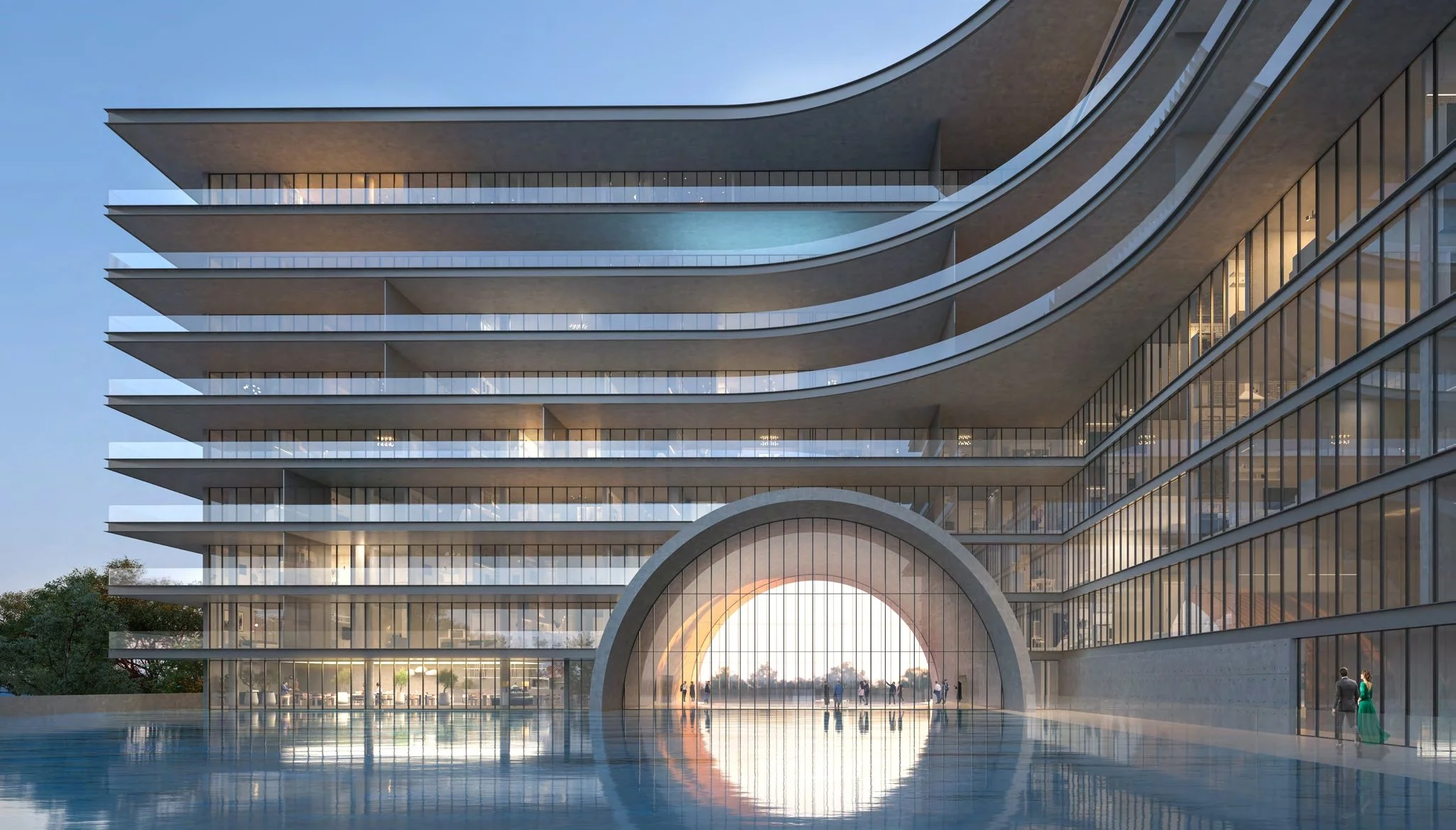 Modern multi-story building with curved balconies, large glass windows, and a circular archway at the entrance reflecting in a pool of water in the foreground.