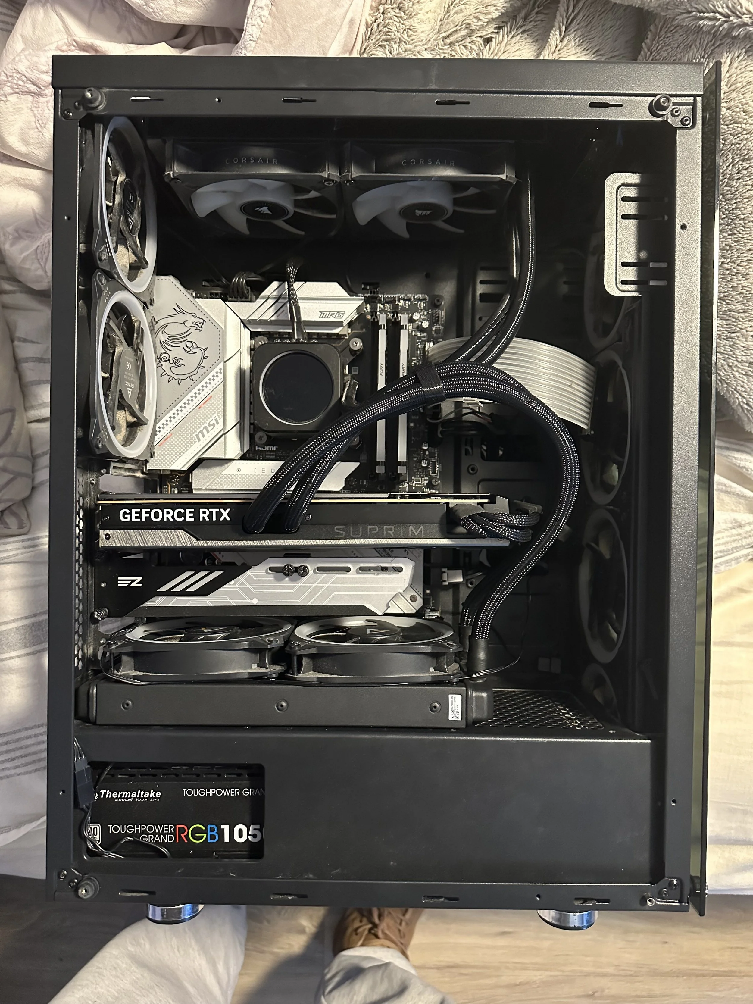 Interior of a custom gaming or high-performance PC build with components including an MSI motherboard, NVIDIA GeForce RTX graphics card, Corsair cooling fans, and a ThermalTake power supply unit, all mounted inside a black case.
