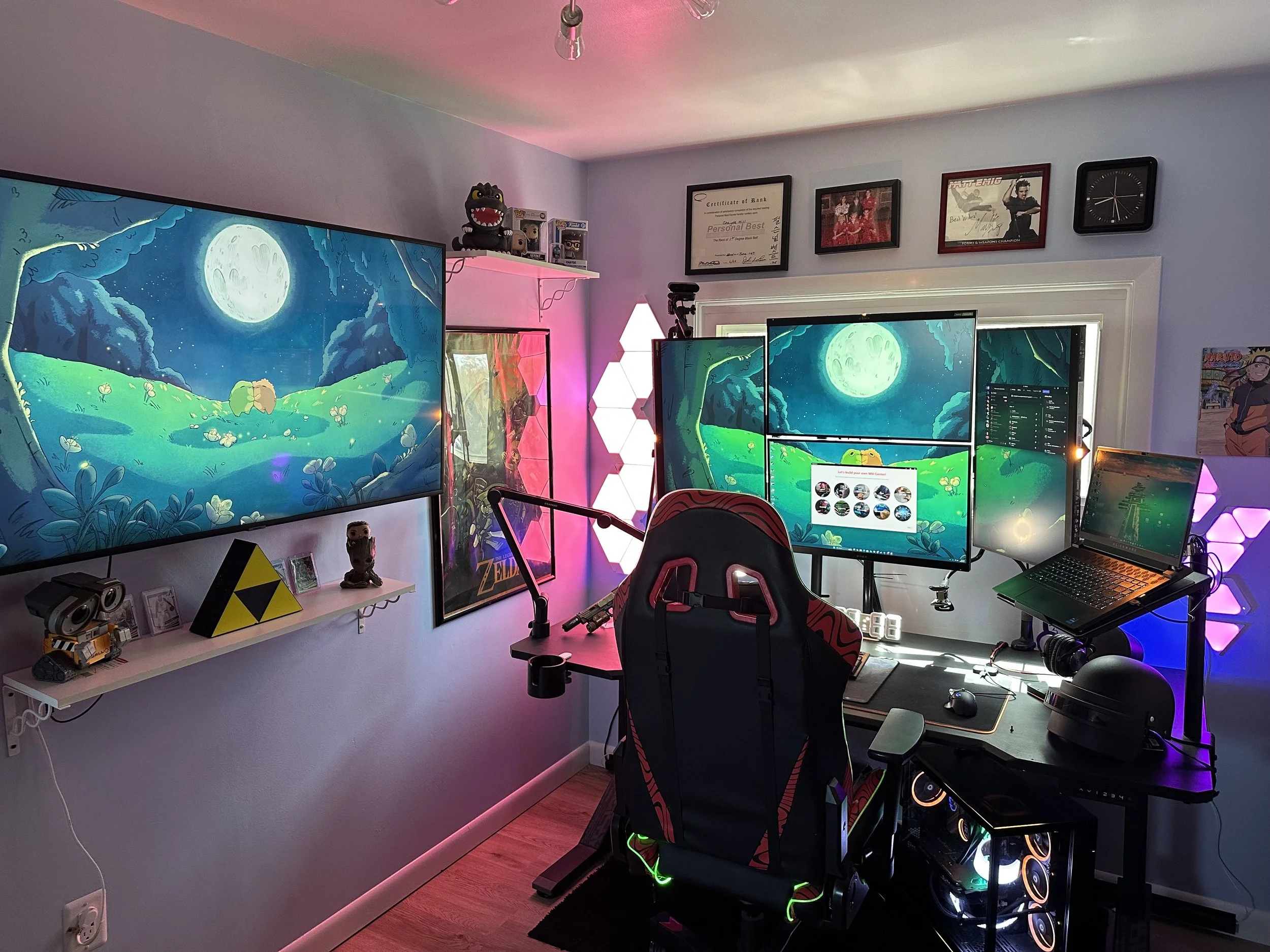 A gaming setup featuring multiple monitors displaying a scene from a cartoon with a full moon and green landscape, behind a gaming chair with a red and black design. The desks hold a keyboard, mouse, and a closed laptop, with RGB lighting and decorative figures on the shelves.