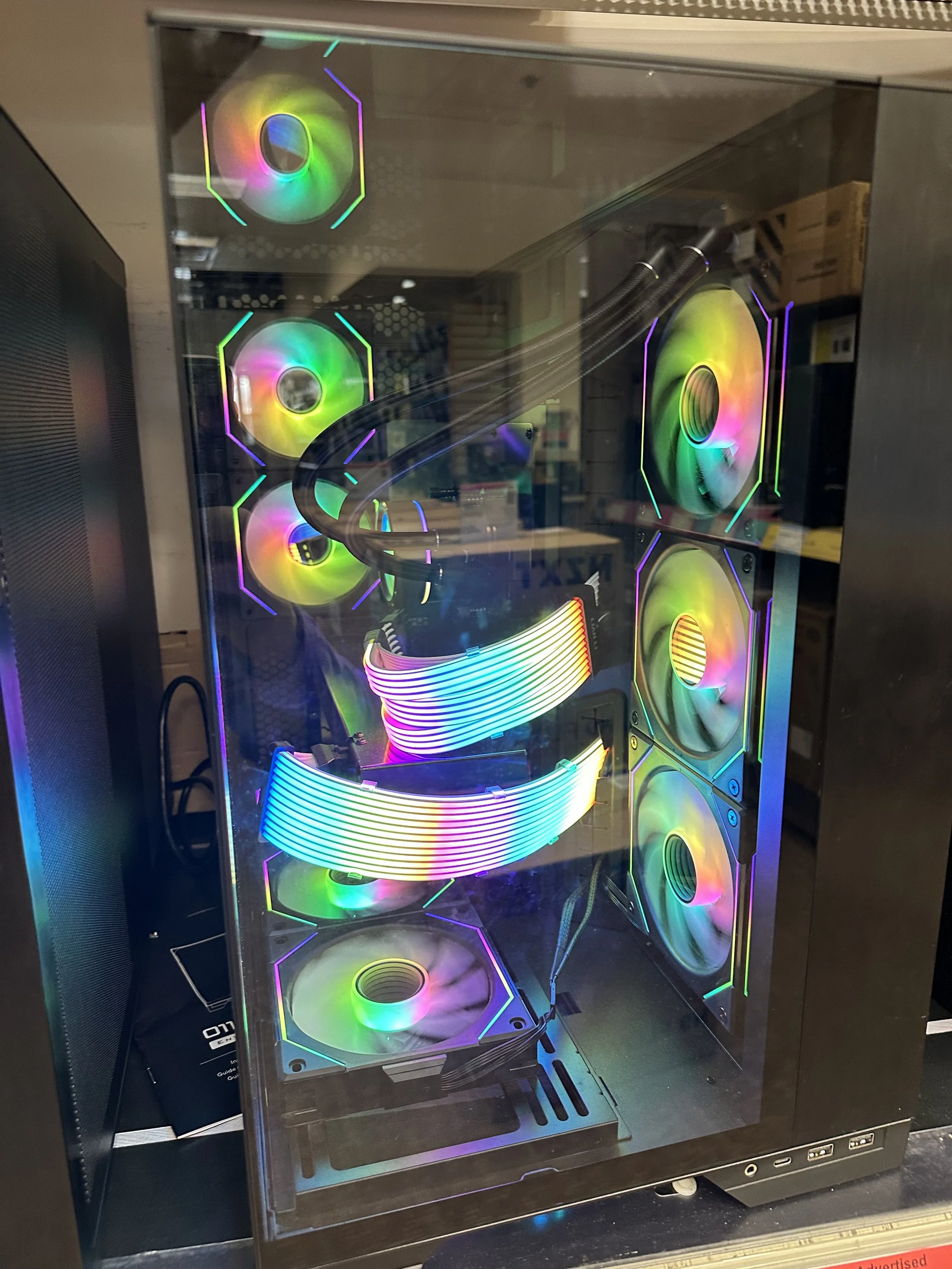 A gaming desktop computer with a glass side panel, featuring multiple RGB case fans, a CPU cooler with RGB lighting, and rainbow-colored LED strips inside.