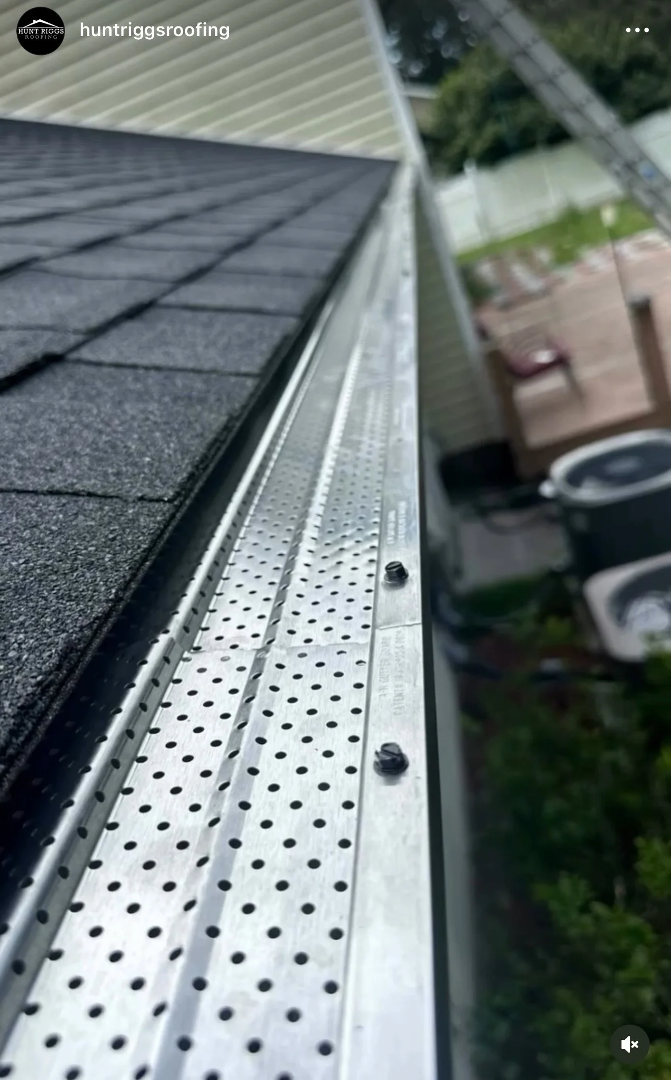 View of house gutter system with black shingle roofing and metal gutters with perforations, close-up perspective.