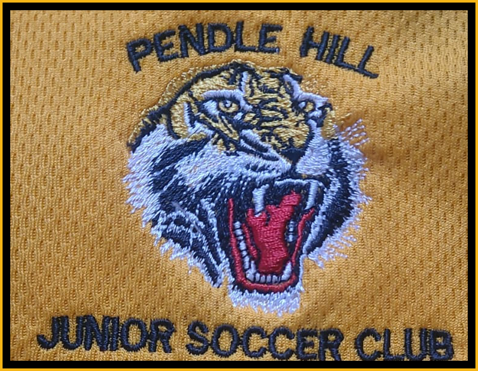Embroidered patch of a tiger's head with open mouth, on a yellow fabric background, with text 'PENDLE HILL' above and 'JUNIOR SOCCER CLUB' below.