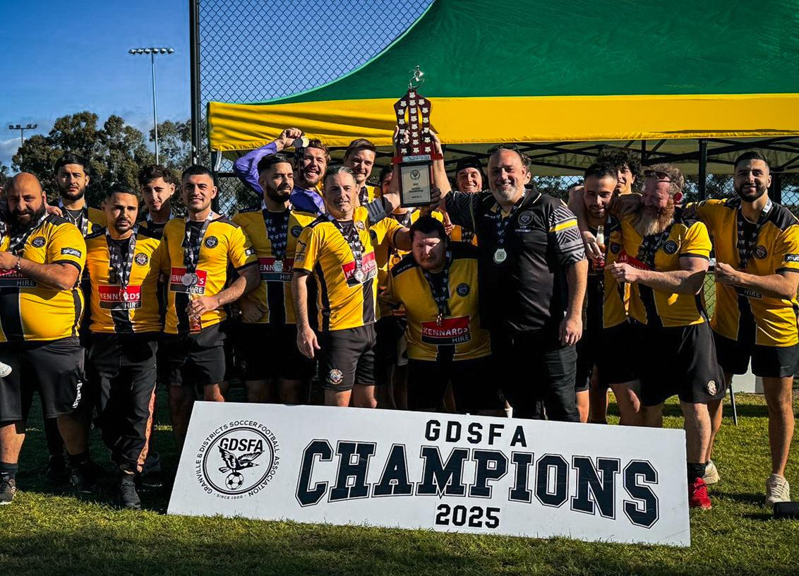A soccer team celebrating their victory, holding a trophy, and standing behind a sign that reads 'GDSFA Champions 2025'. They are wearing yellow and black jerseys, and the scene is outdoors on a soccer field.