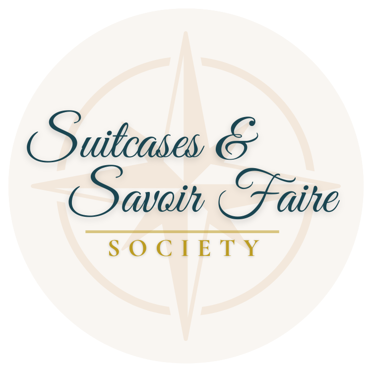 Logo for Suitcases & Savoir Faire Society featuring a compass rose in the background, with elegant script text over it.