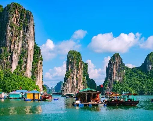 boats on a body of water with tall limestone islands covered in greenery under a blue sky with white clouds