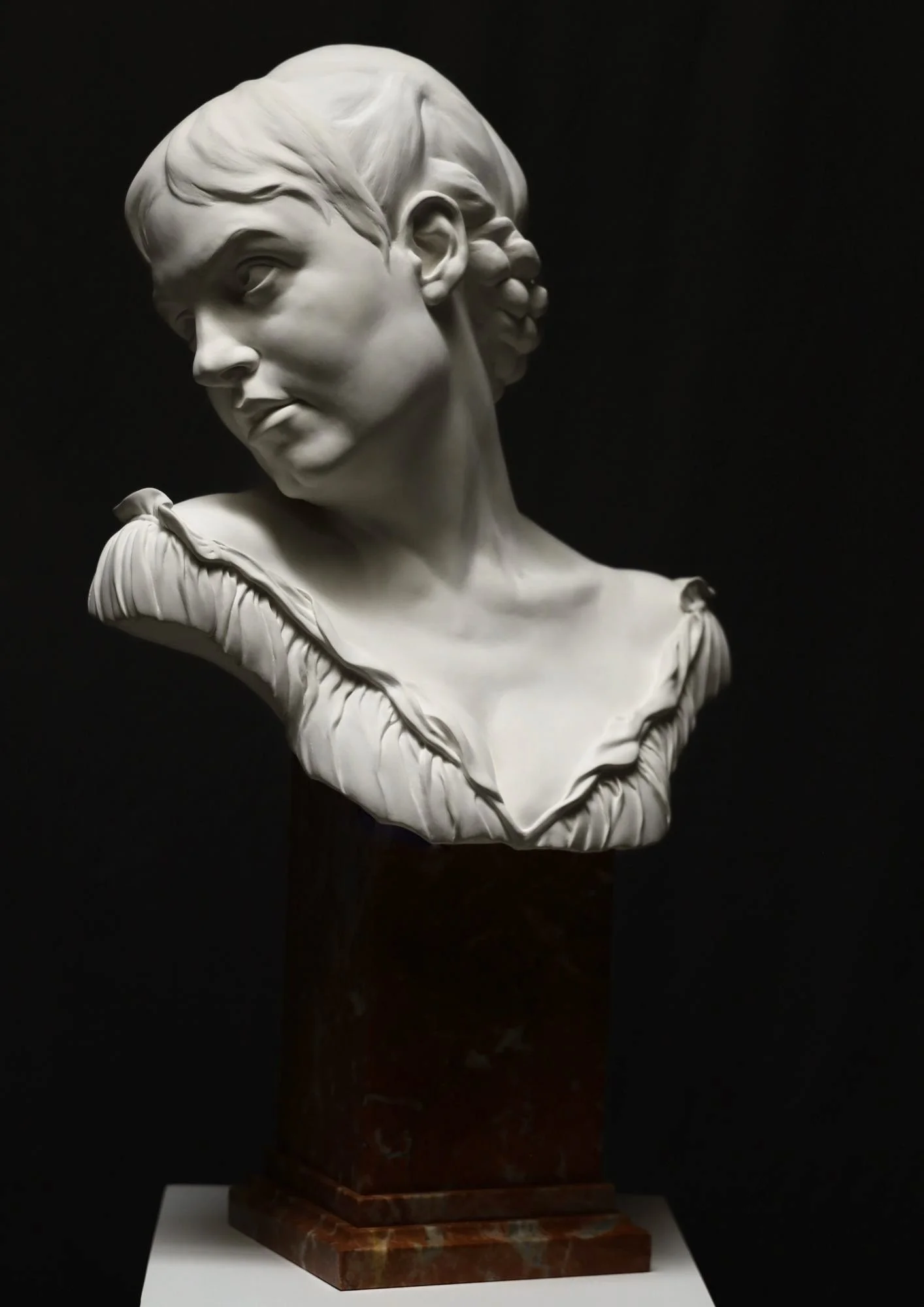 Marble bust sculpture of a woman with a side profile view against a black background.