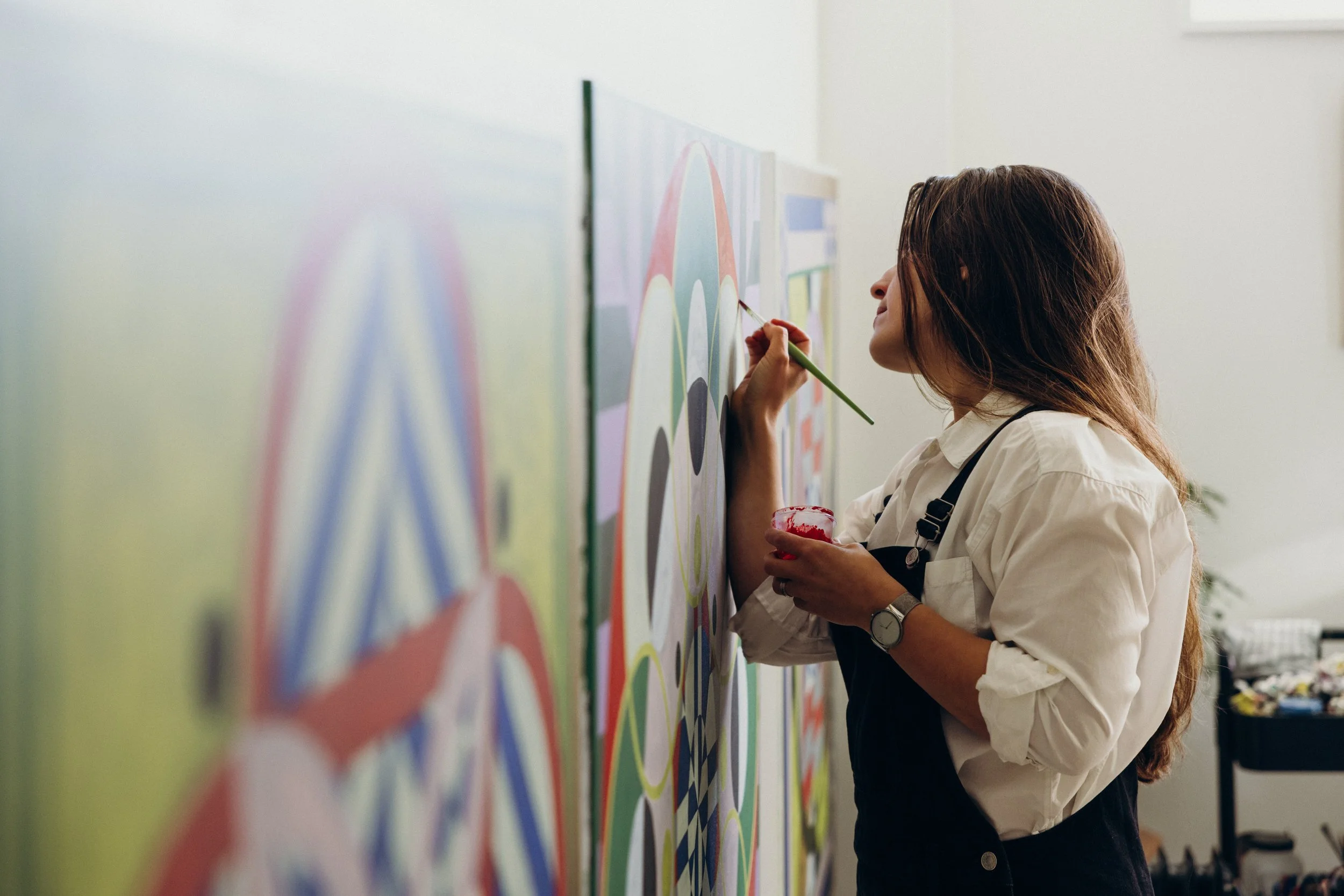 Kate painting in her studio, with an abstract painting seen from the side in the foreground. Photo by Nick George