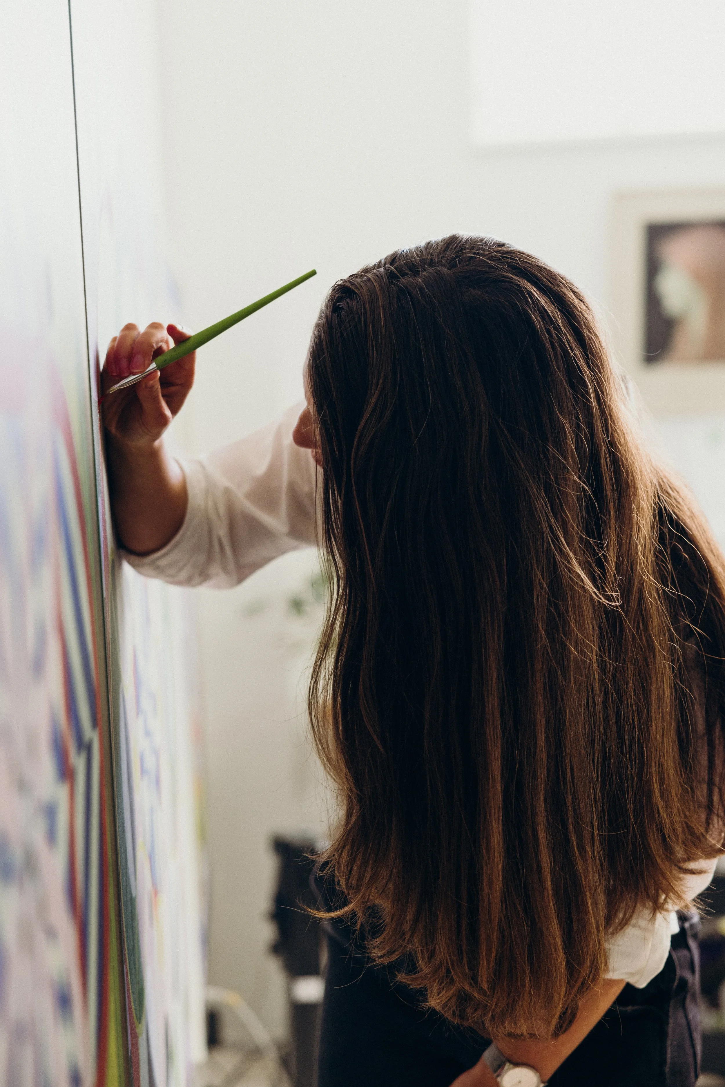 Kate in her art studio, seen from the side working on a painting with a paint brush. Photo by Nick George