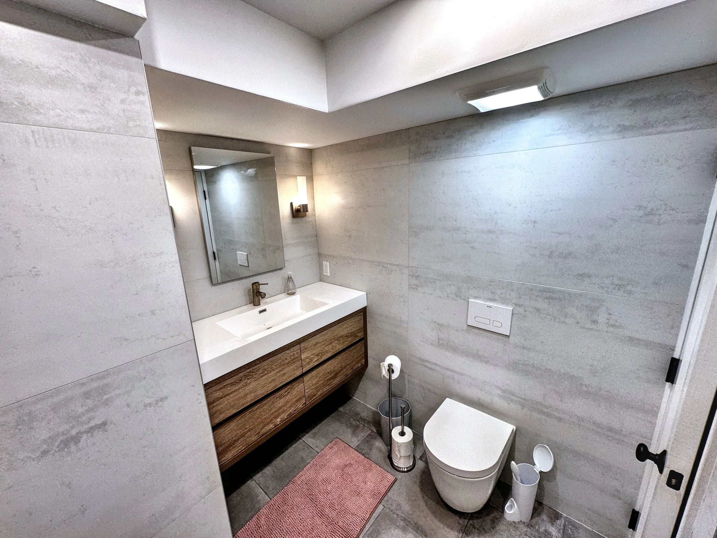 Modern bathroom with a wall-mounted vanity, sink, large mirror, toilet, and minimal decor.