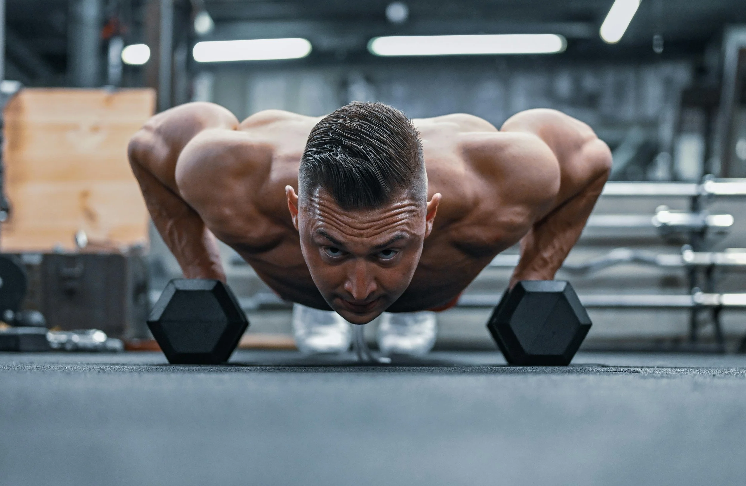A shirtless man is doing push-ups with dumbbells on a gym floor.