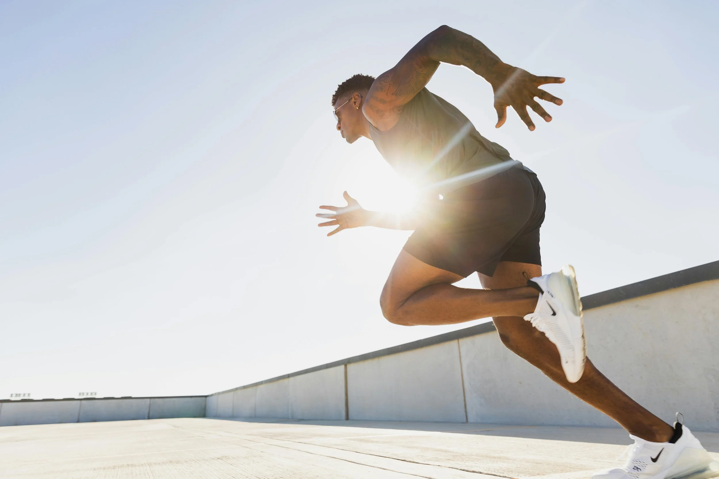 A male athlete in a sprinting position on a track, with the sun shining behind him and a clear sky above.